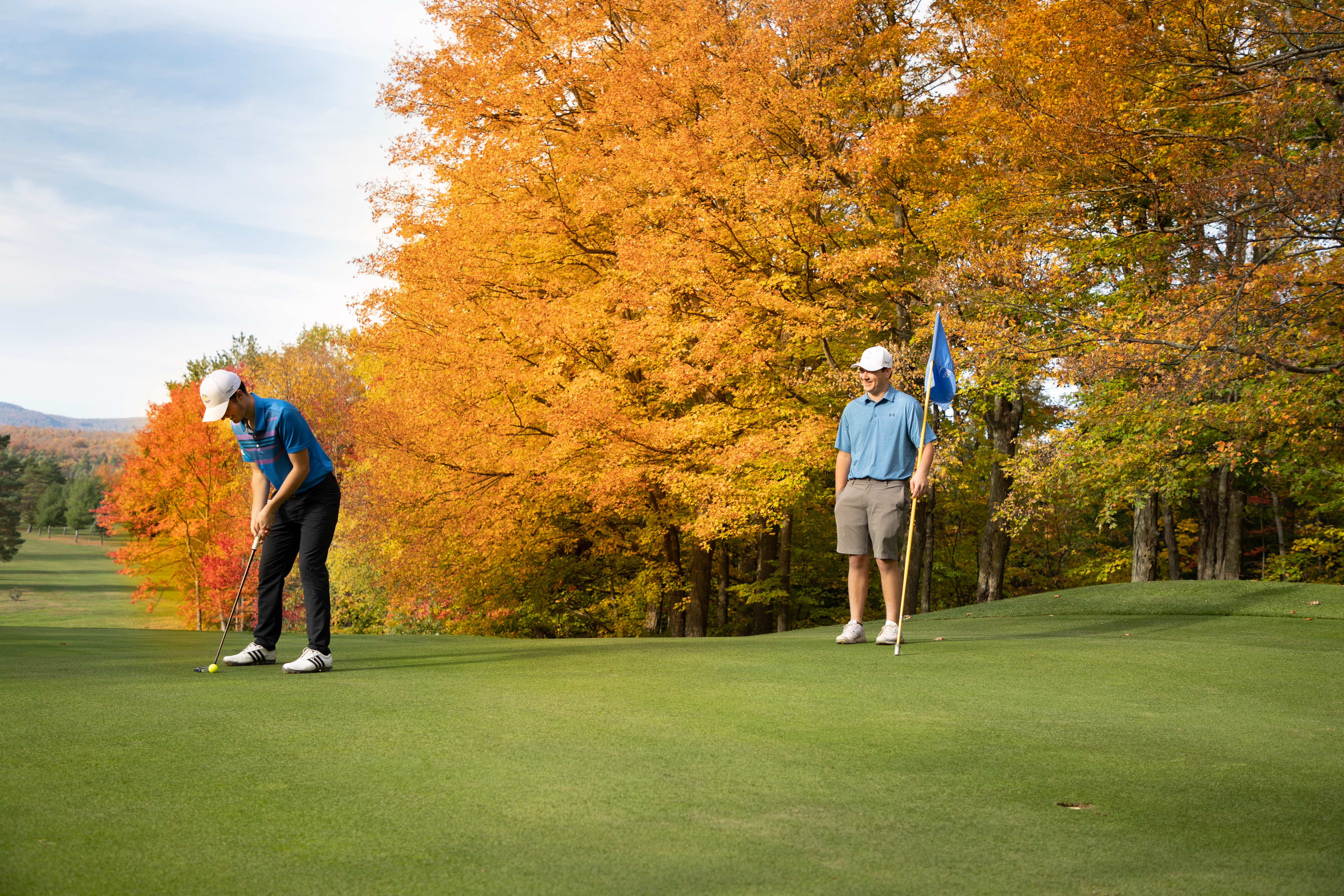 Two men play golf among foliage. 