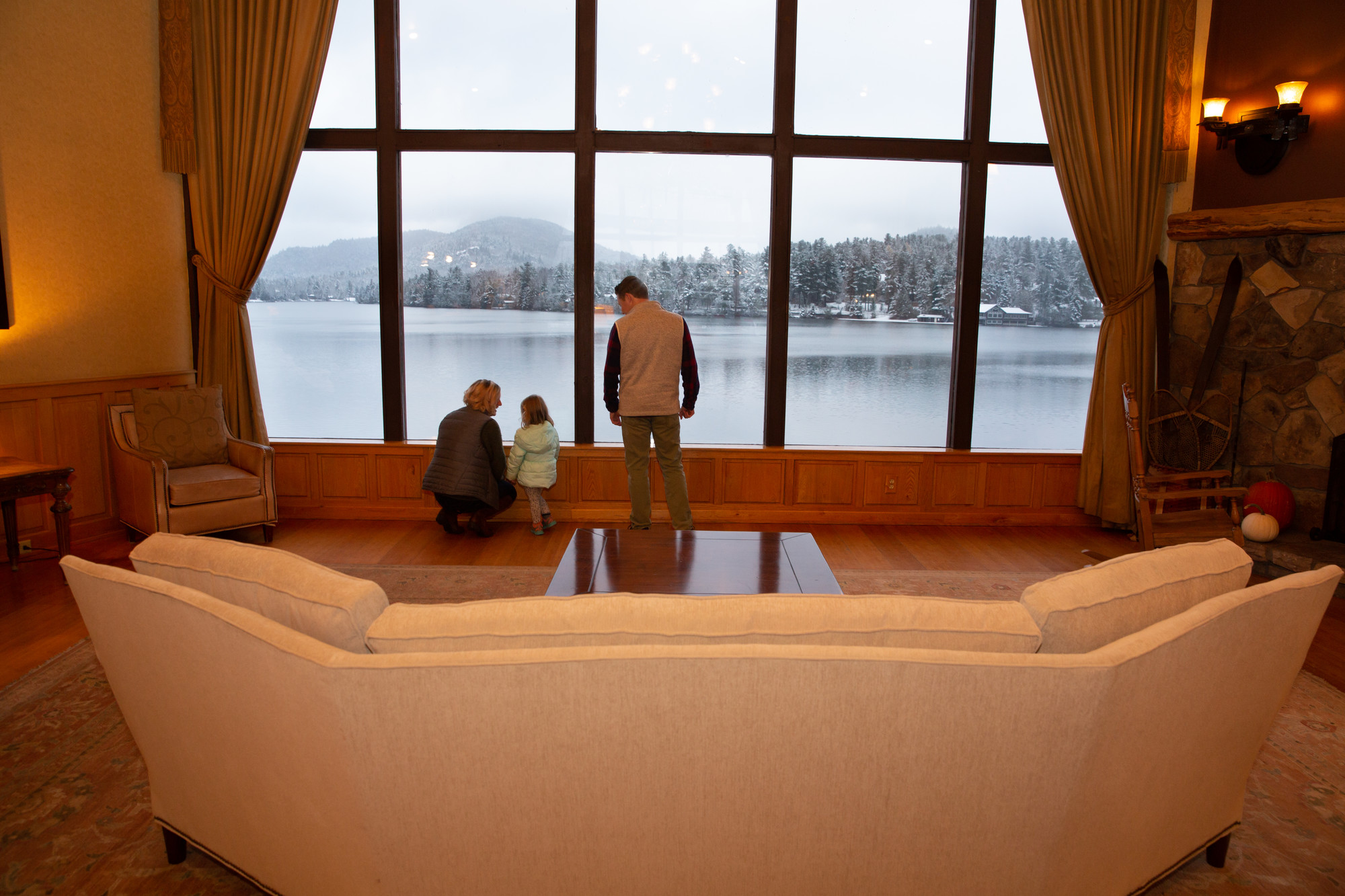 A man, woman, and small child look out at a lake through two-story windows.
