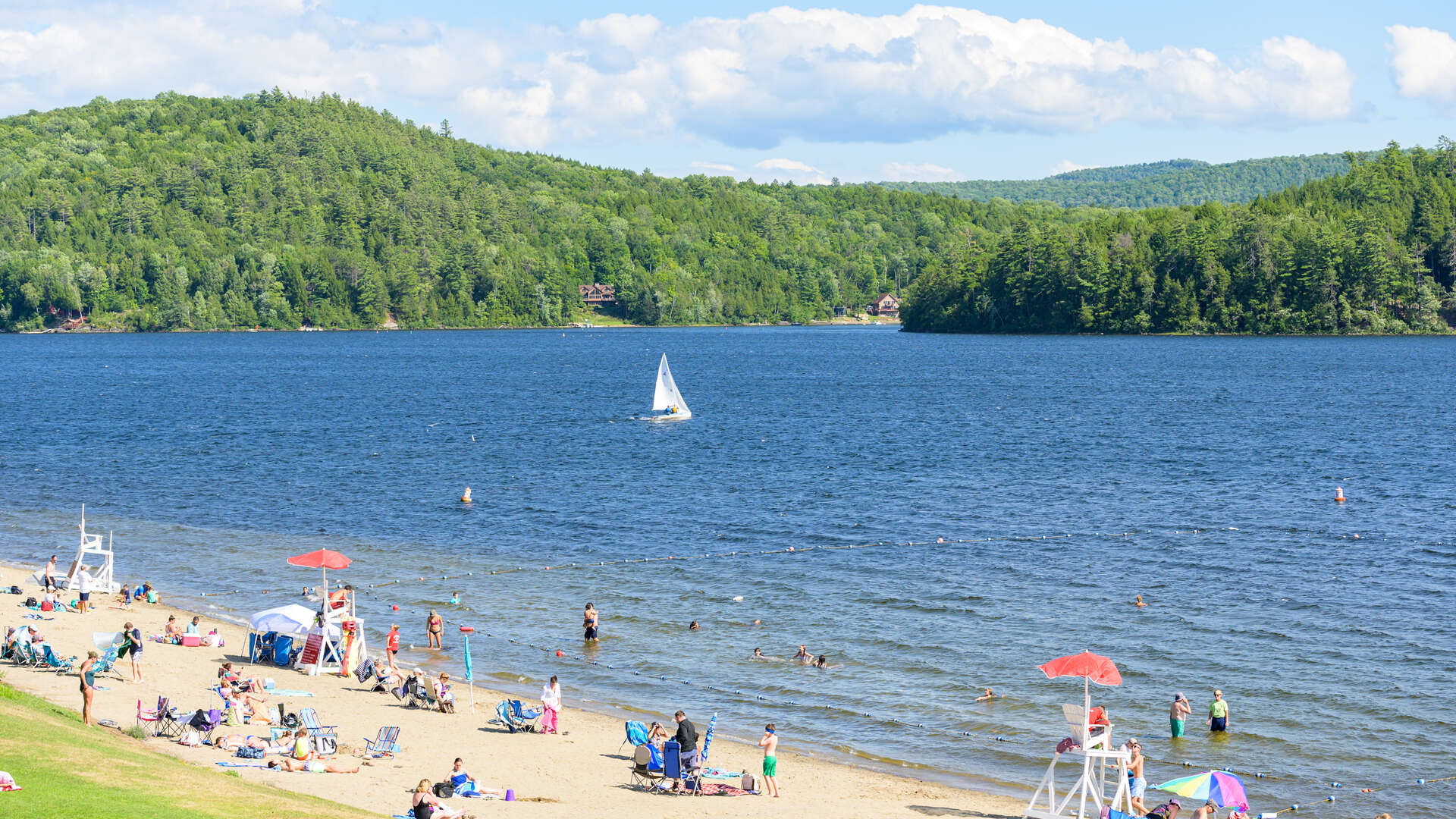 People sitting on a beach overlooking Schroon Lake. 