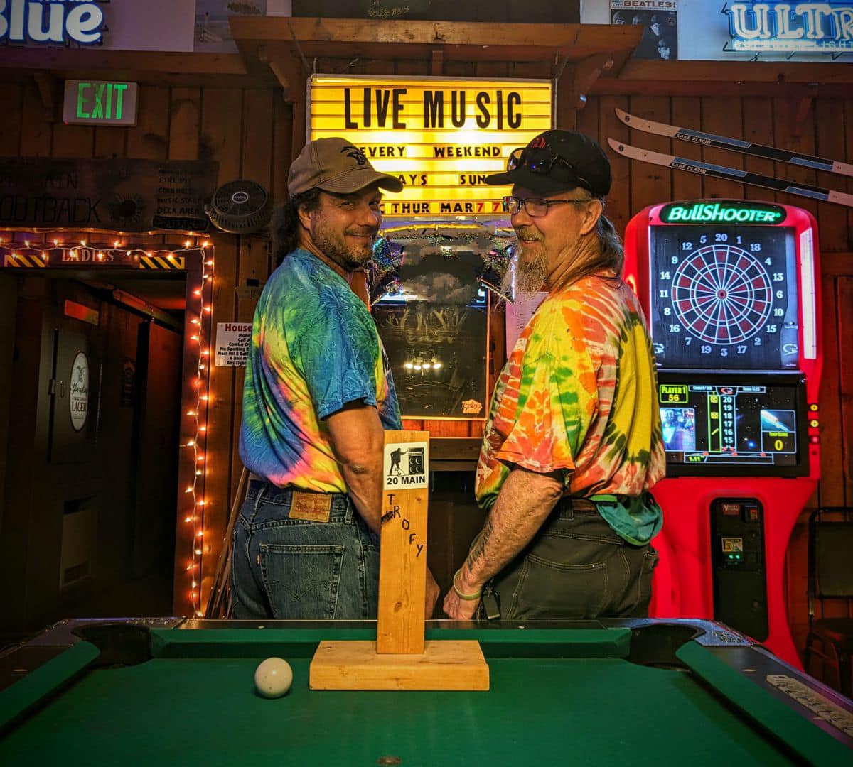 Men in tie-dye shirts pose with trophy at pool table