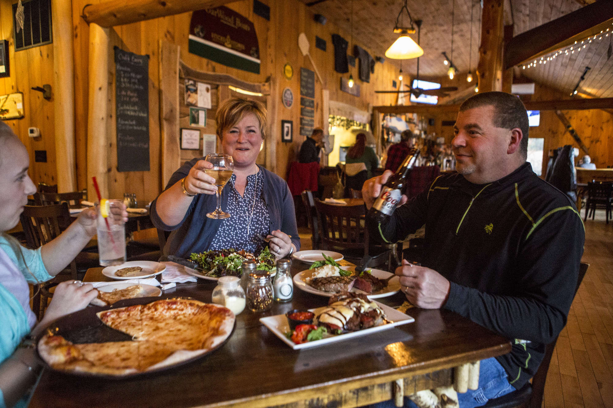 A family of three cheerses in a restaurant with wood interior.