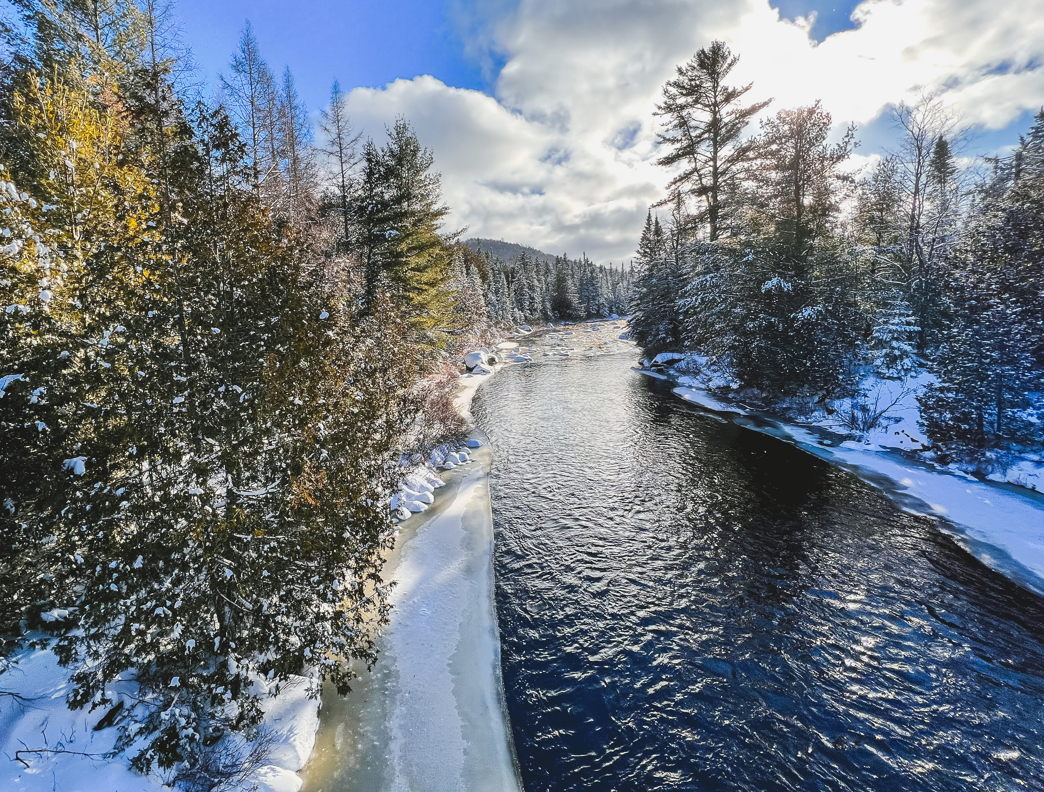 A river with a snow-covered bank and a hill in the distance.