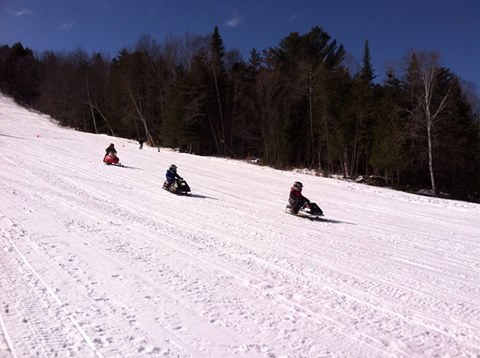 Three snowmobiles race on a groomed trail.