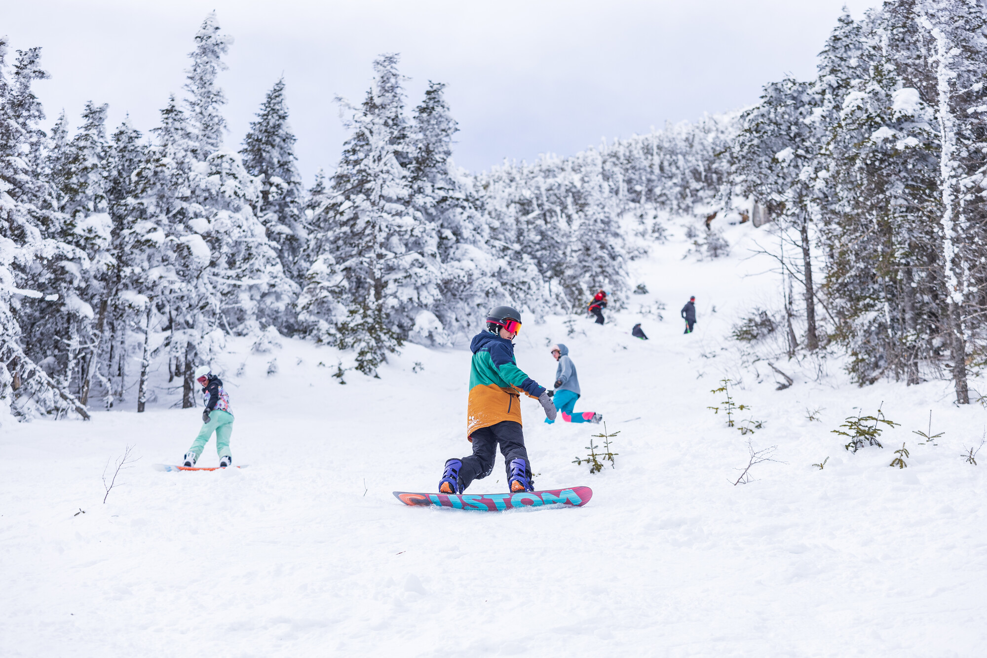 A group of snowboarders riding down a snowy slope at Whiteface Mountain.