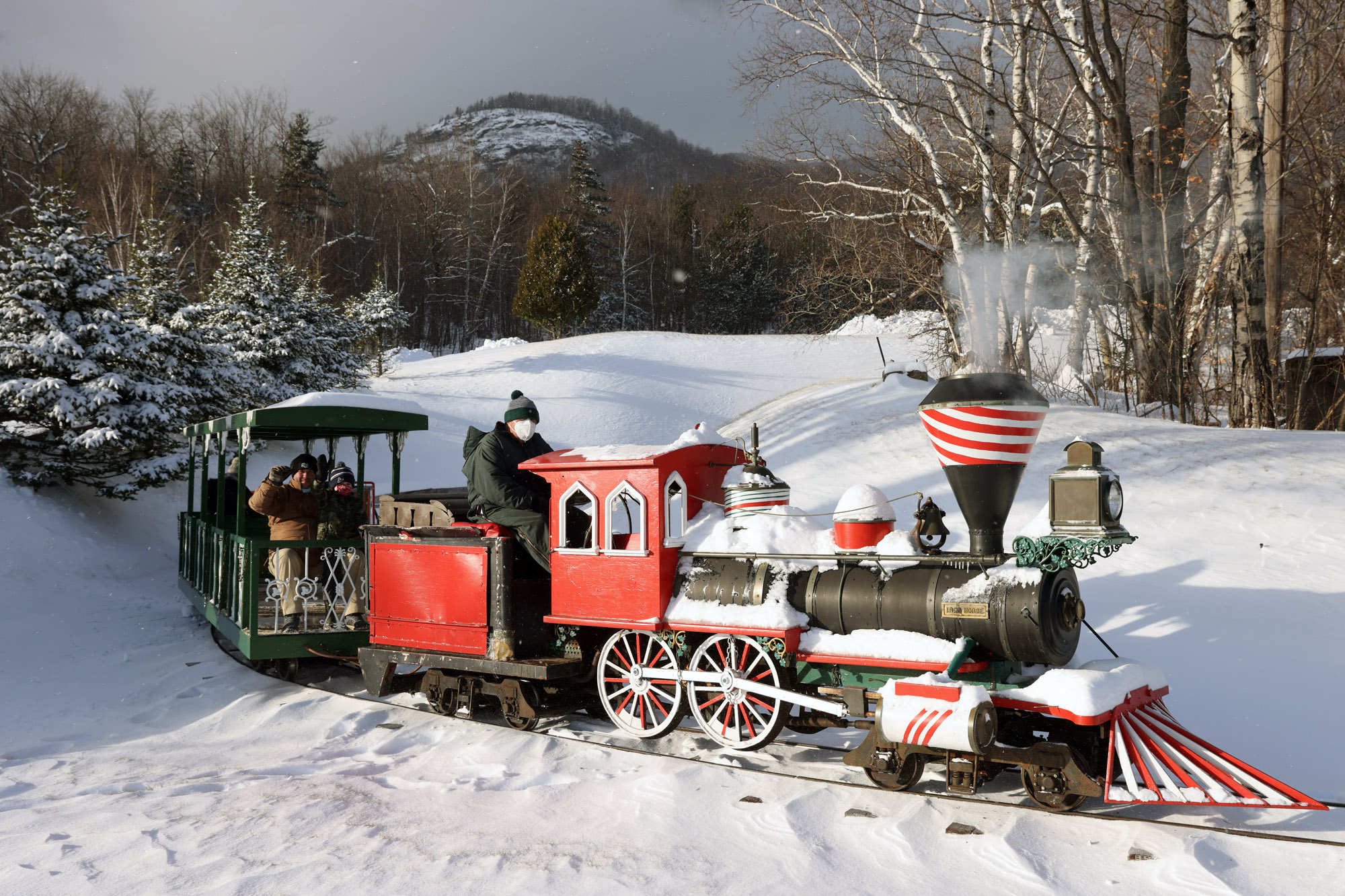 A small train rides tracks across a snowy landscape with a mountain in the background.