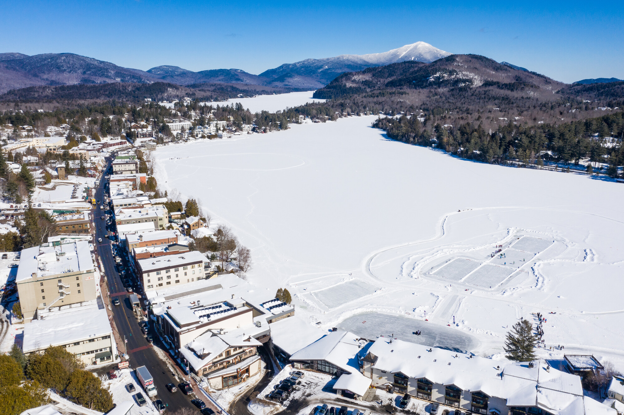 An aerial shot of lake placid in winter with a frozen lake and mountains in the background. 