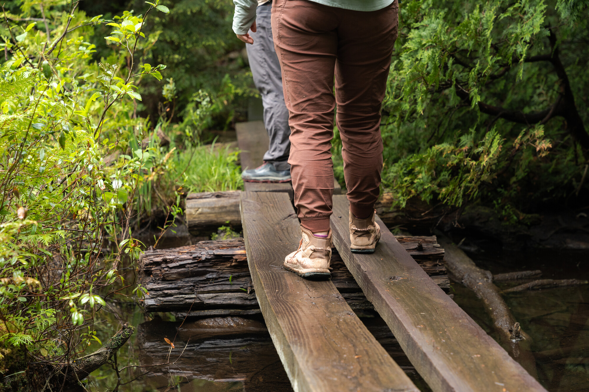 Two pairs of feet wearing hiking shoes walking across wet wooden boards