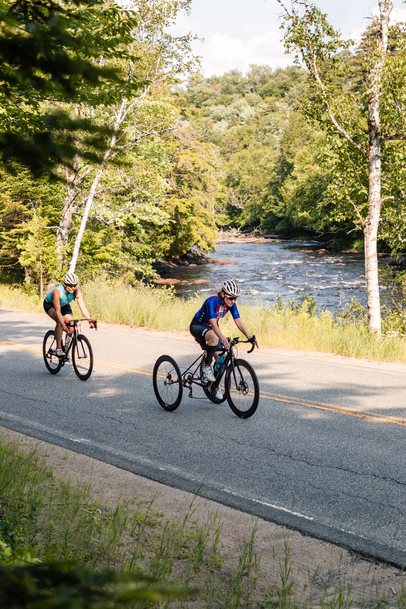 A paracyclist and her friend bike along a river.