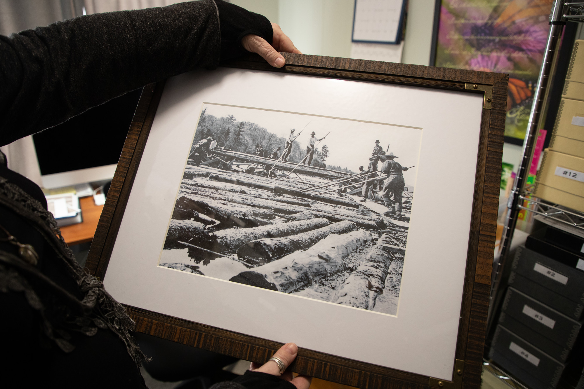 A person's hands hold a printed photo of a historic logging operation