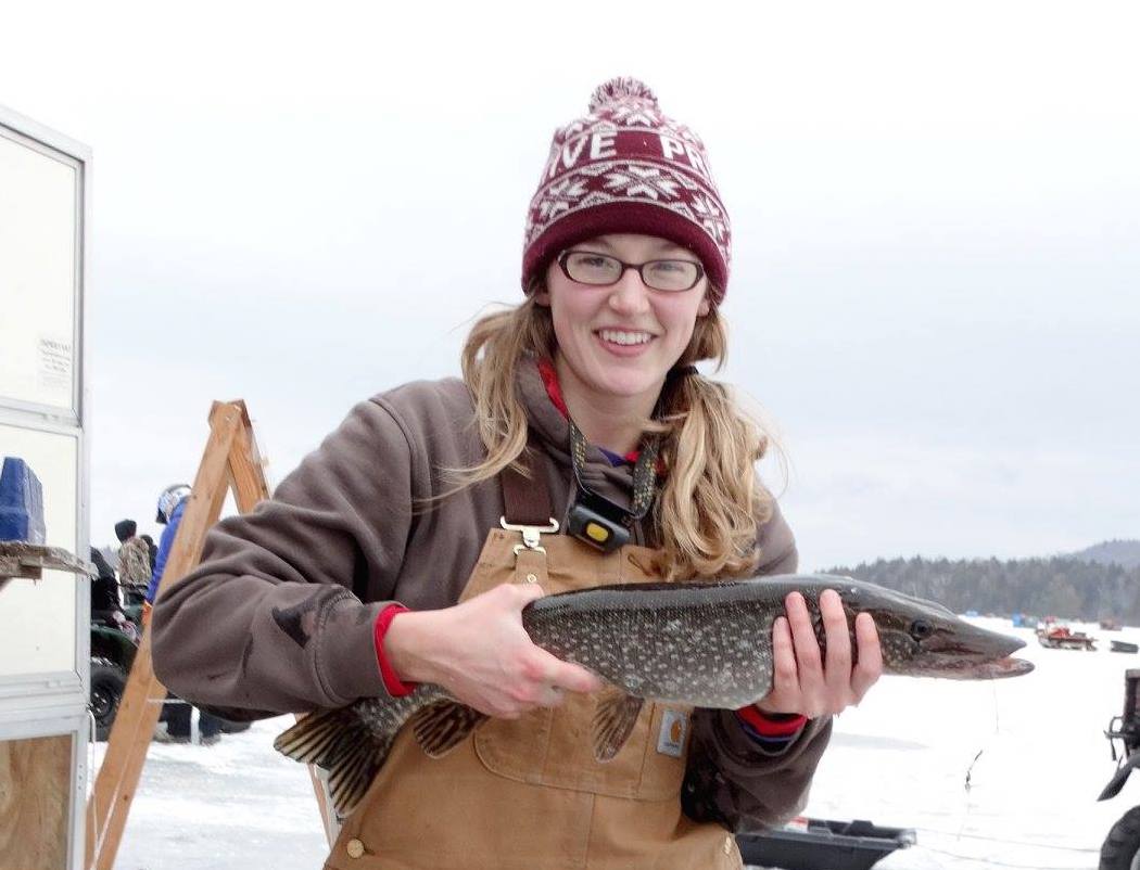 A woman poses on the ice with a caught fish. 