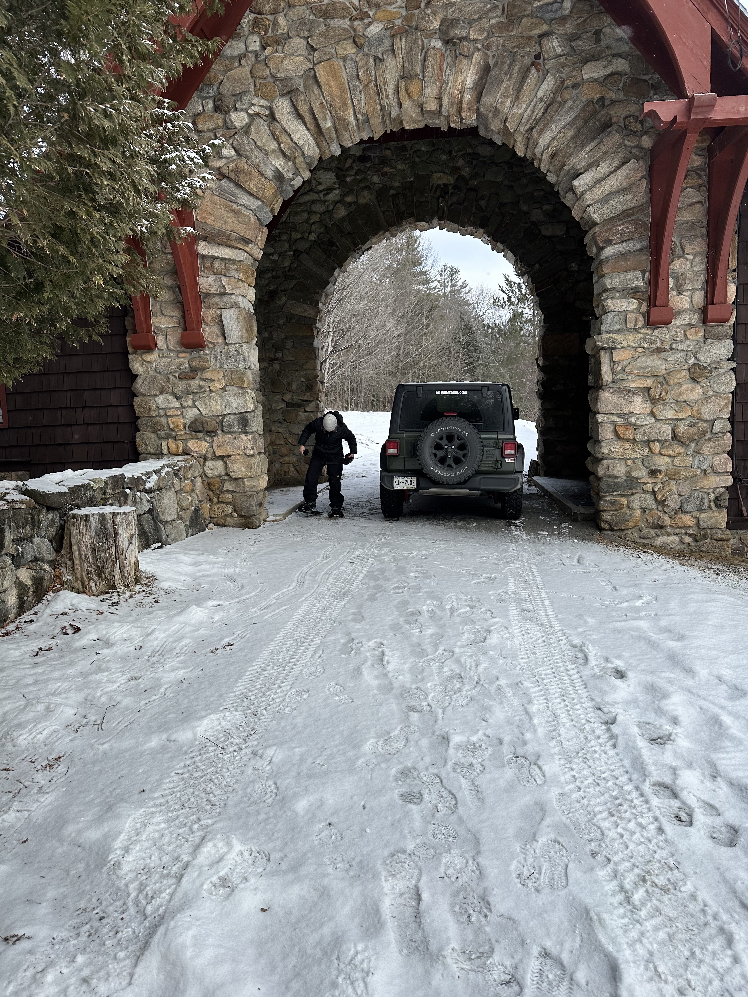 A woman straps into snowshoes next to a stone carriage house.