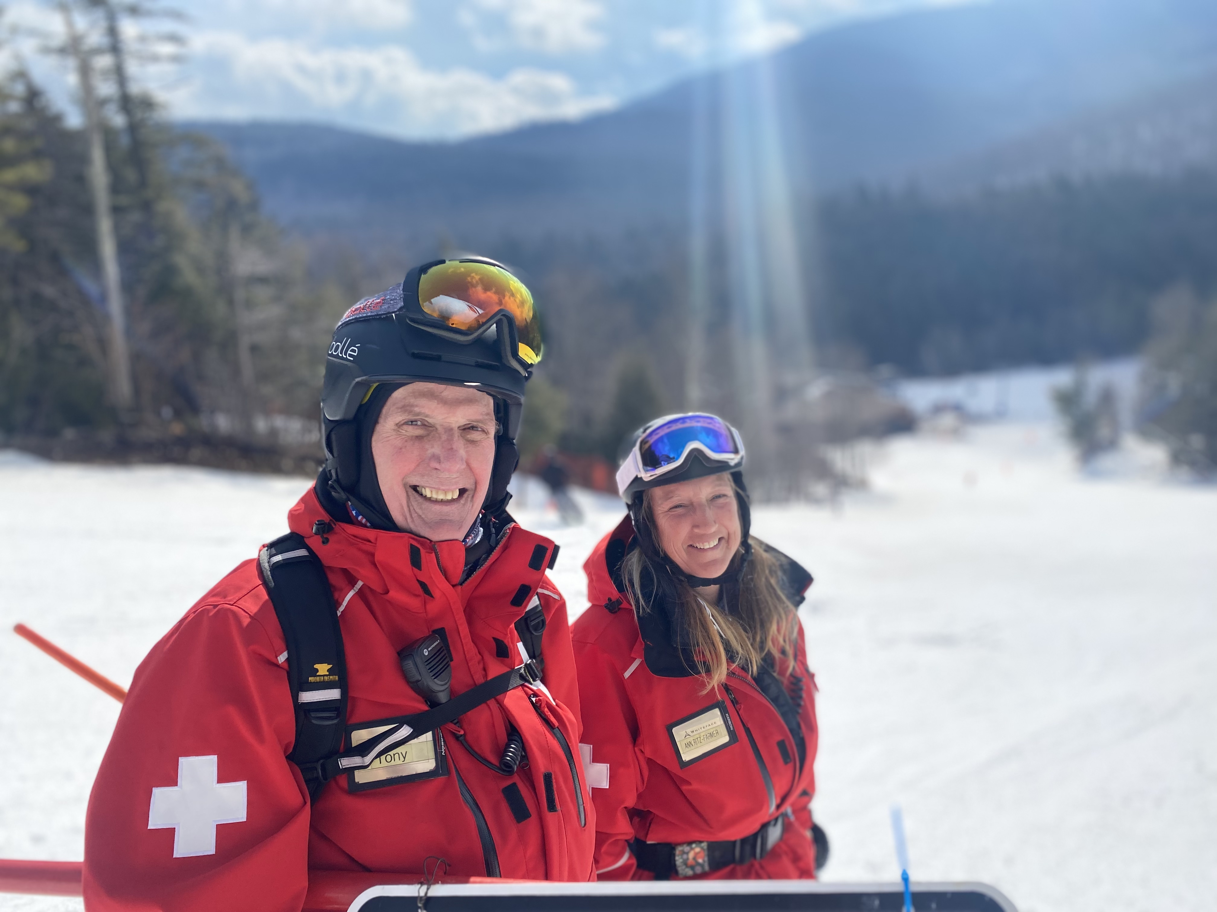 Tony and Ann smiling in their ski patrol jackets as they put up signage along the trail