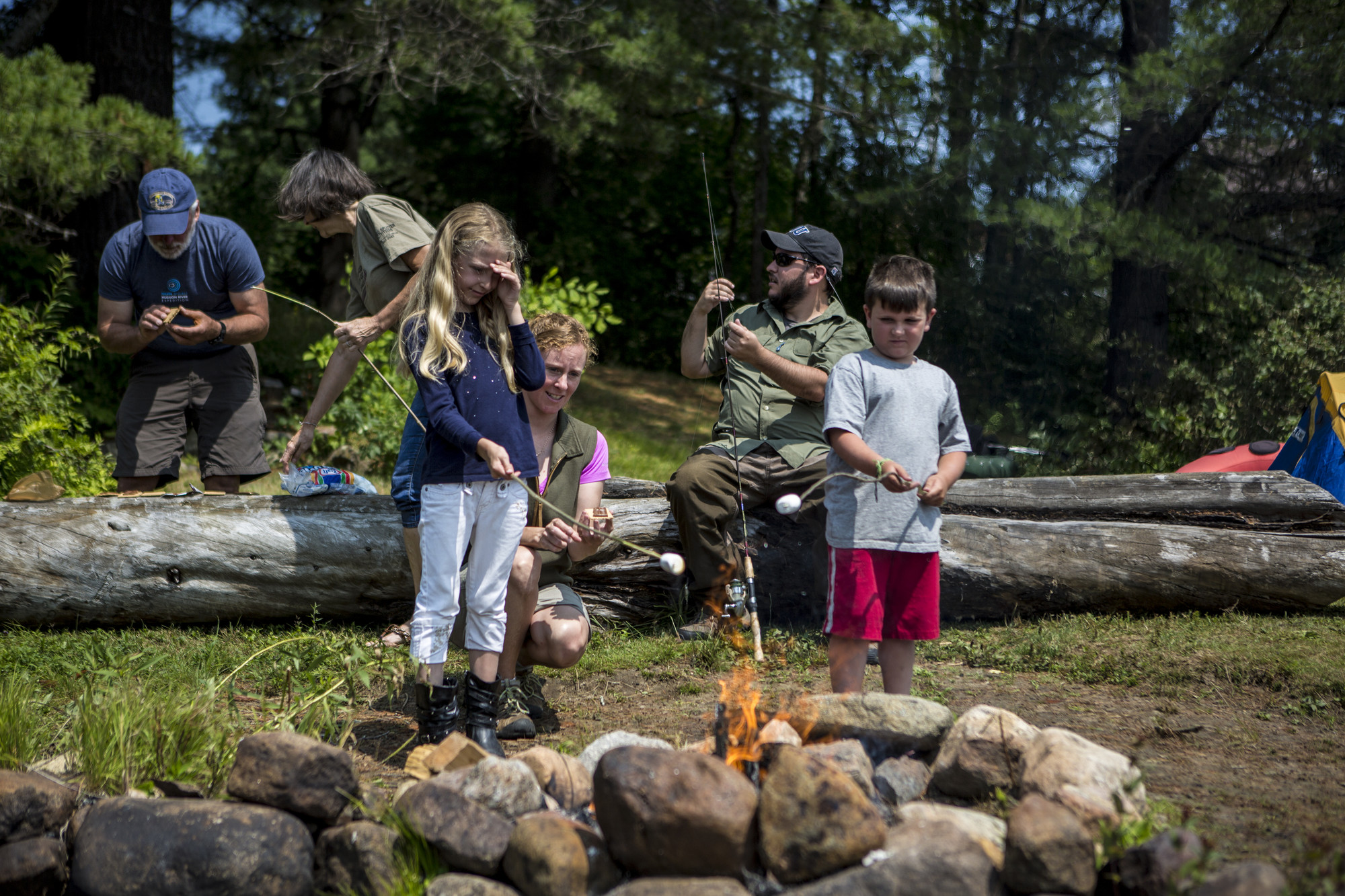 Kids, parents, and grandparents roasting marshmallows by a fire.