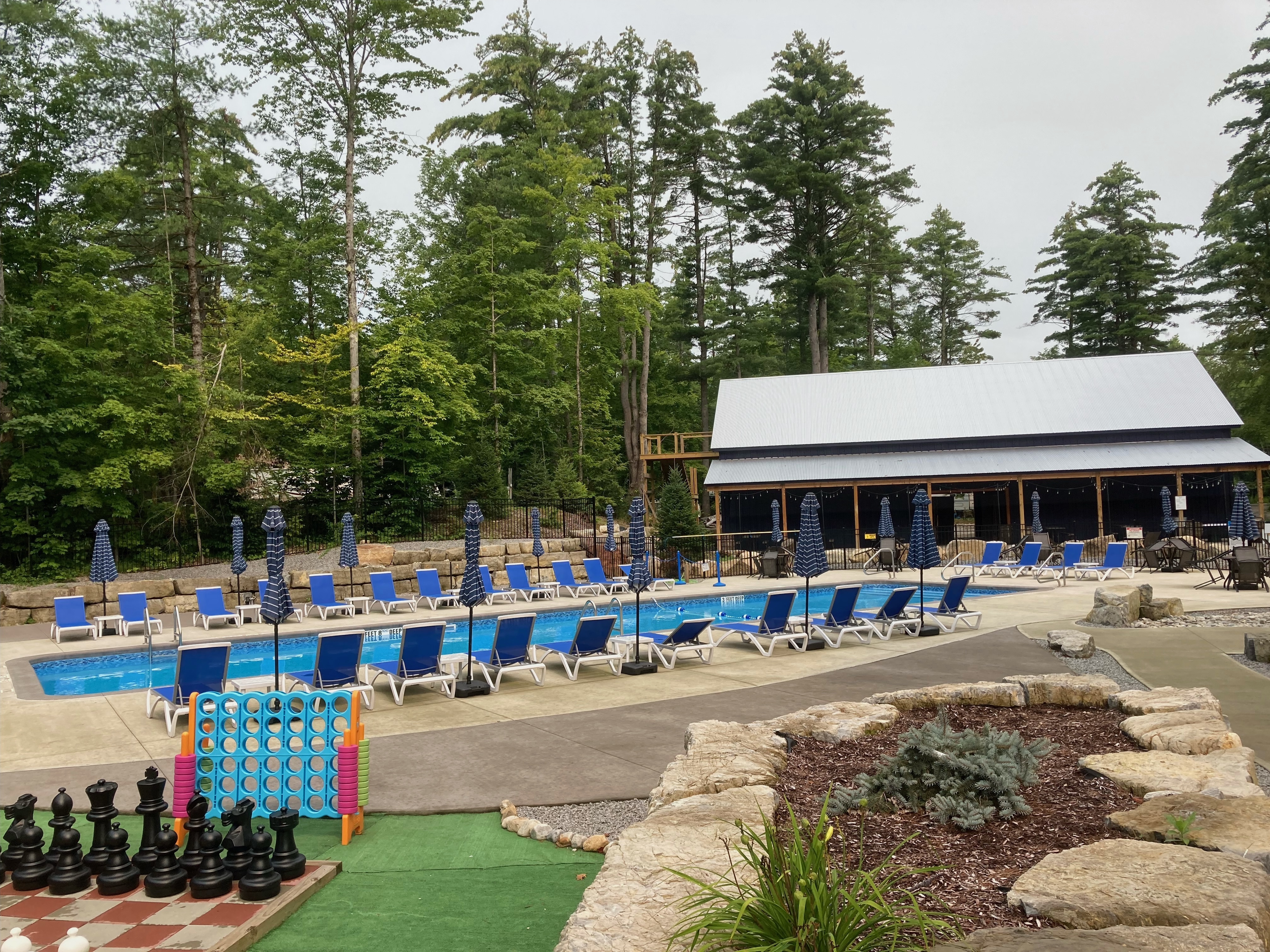 An inground pool with beach chairs around it and a pool house in the back. 