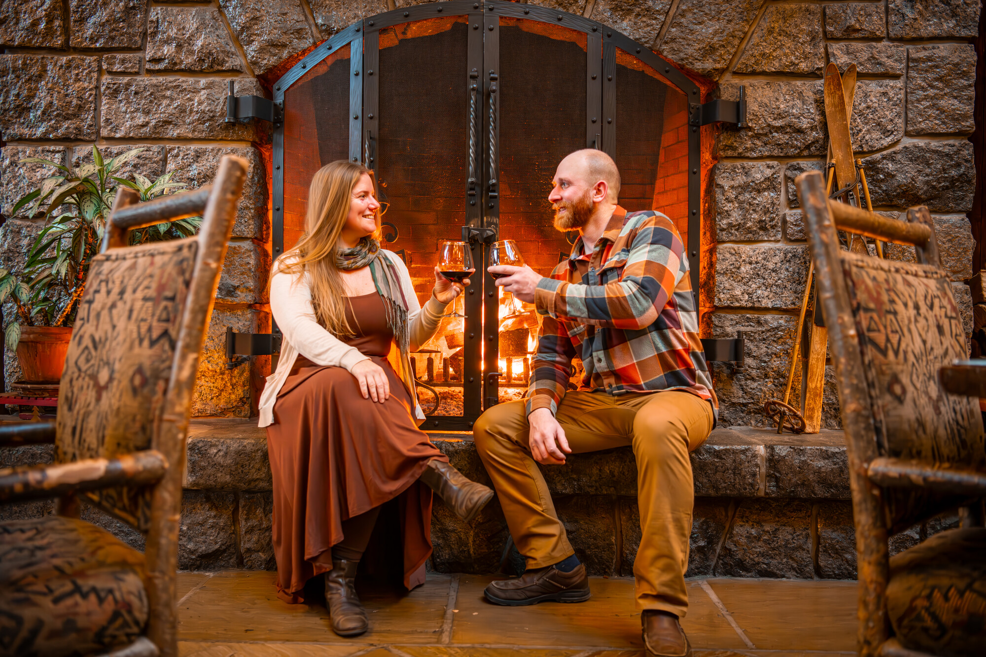 A man and woman share a glass of whine by a fireplace. 