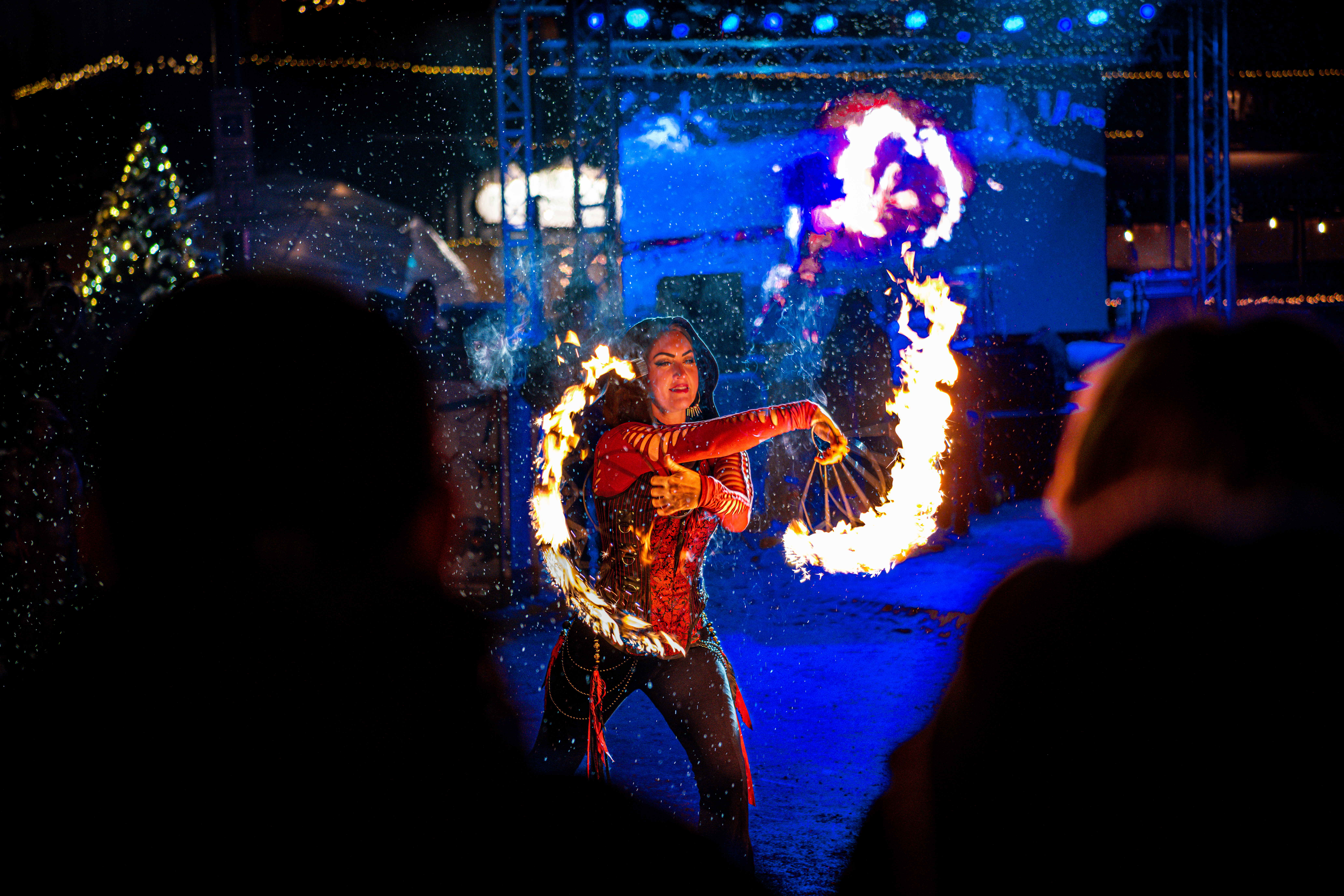 A dancer twirls flaming sticks in front of a crowd at night.