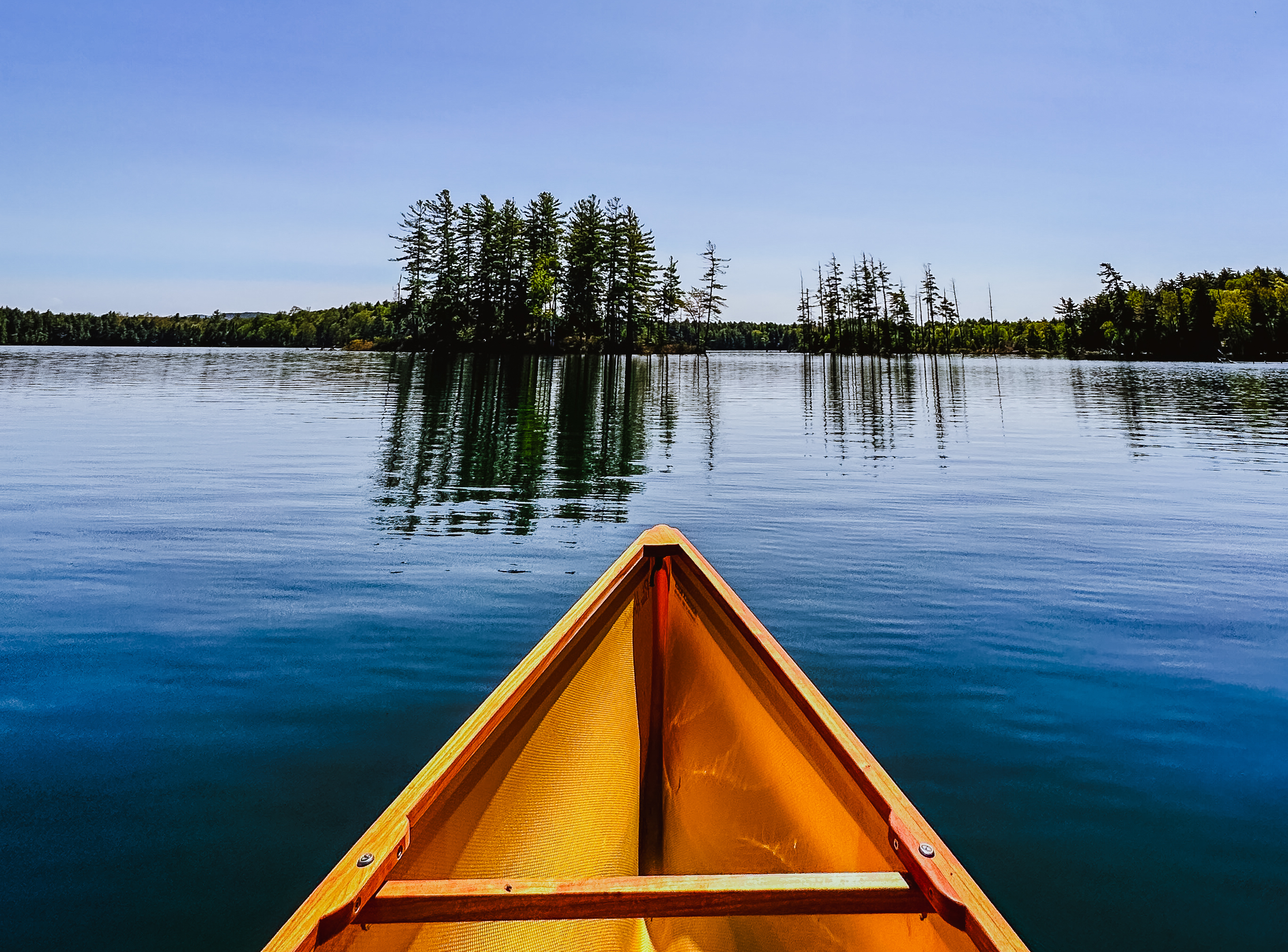 Little Clear Pond. The bow of a canoe on a placid pond with two small islands directly in front.