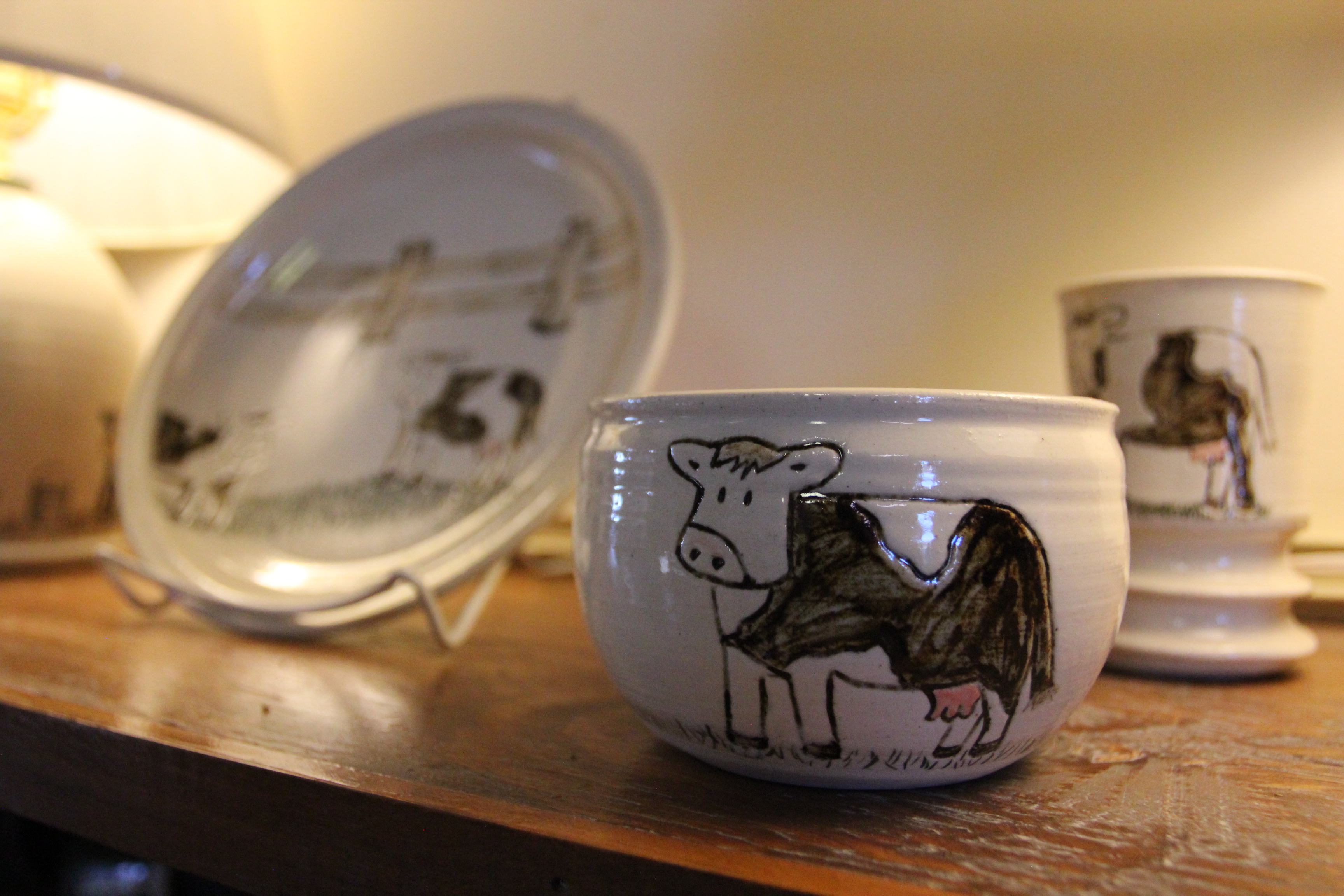 A ceramic set include a bowl, plate, and cup decorated in loosely drawn cows. 