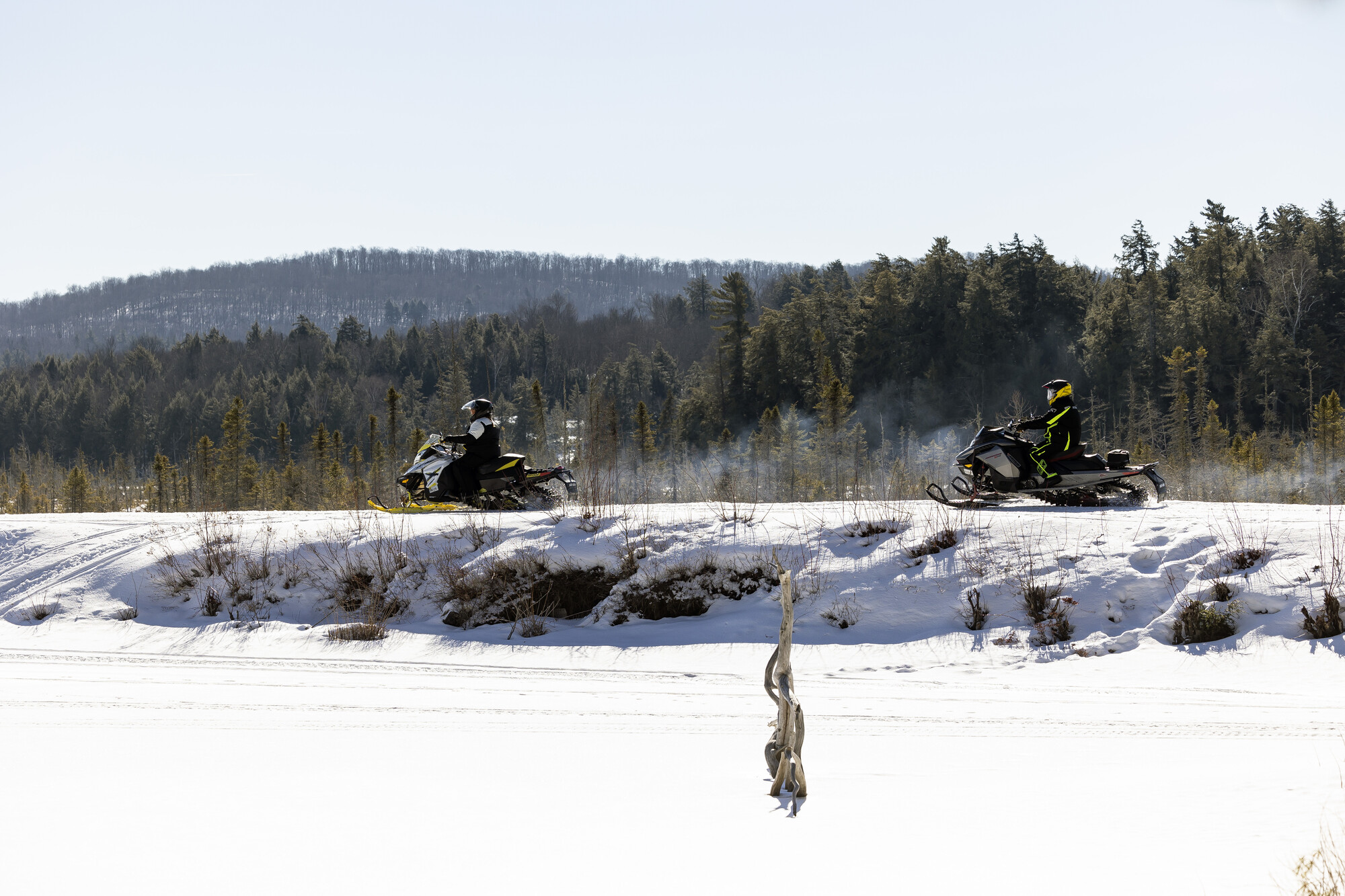 Two snowmobilers ride on a snowy straight-away. 
