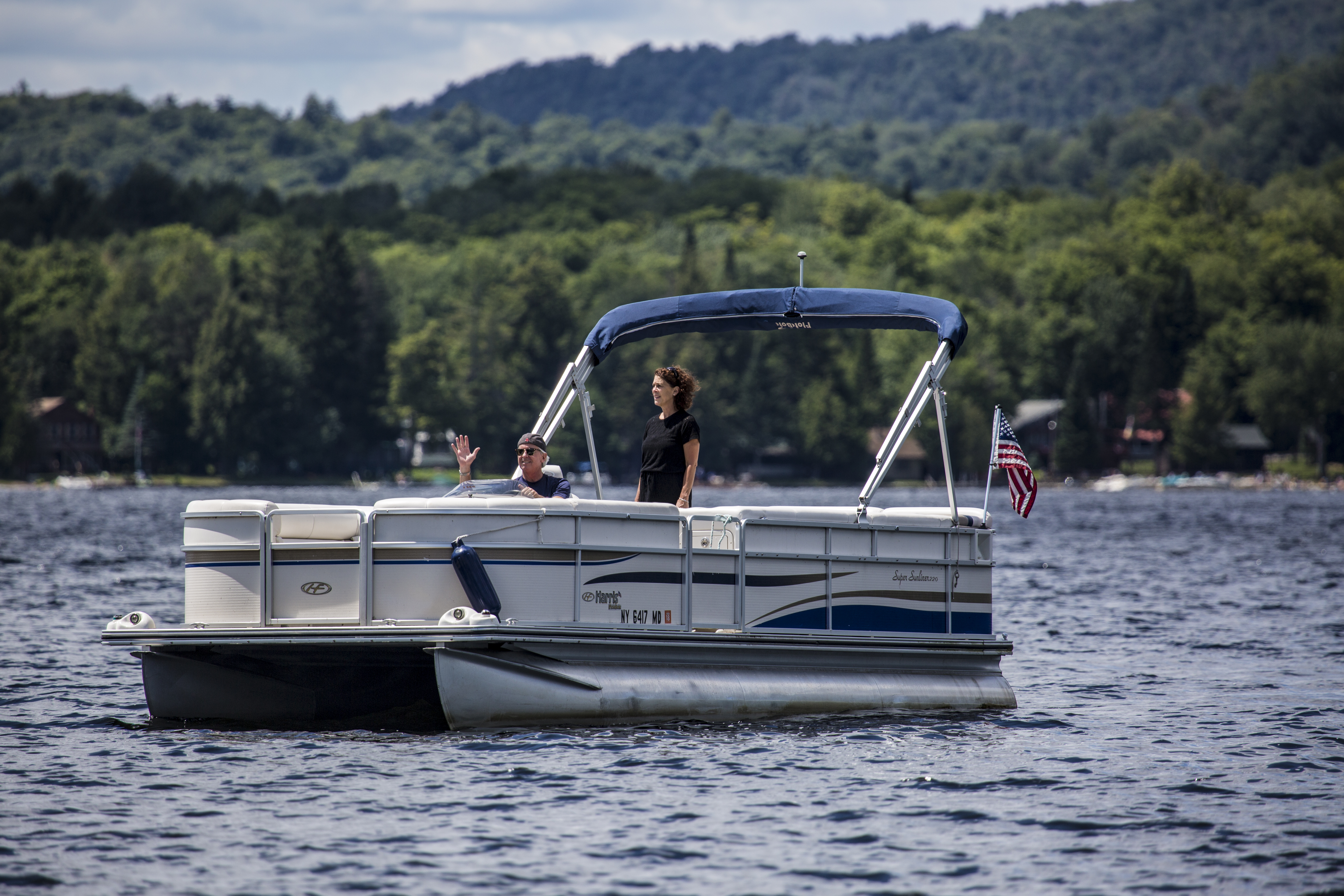 A couple on a pontoon boat with tree-lined shore in the background.
