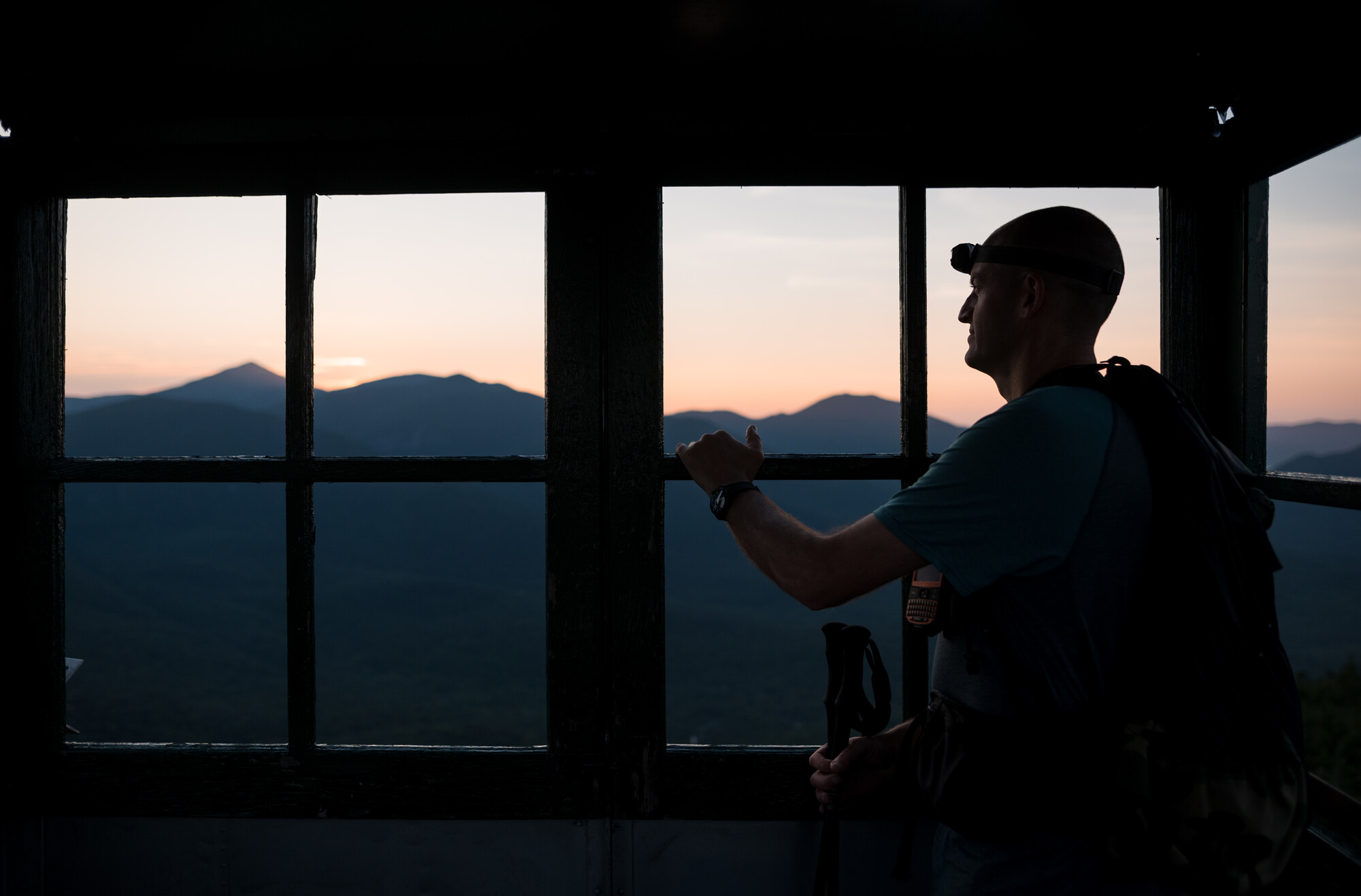 A man looks out of the Mount Adams fire tower window at sunrise