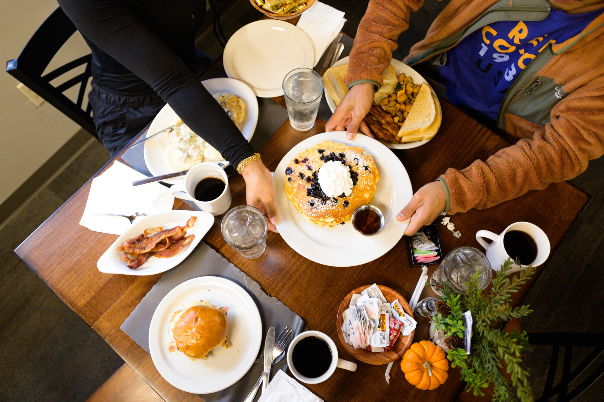 Looking down at a table with breakfast food, blueberry pancakes with syrup, and coffee.