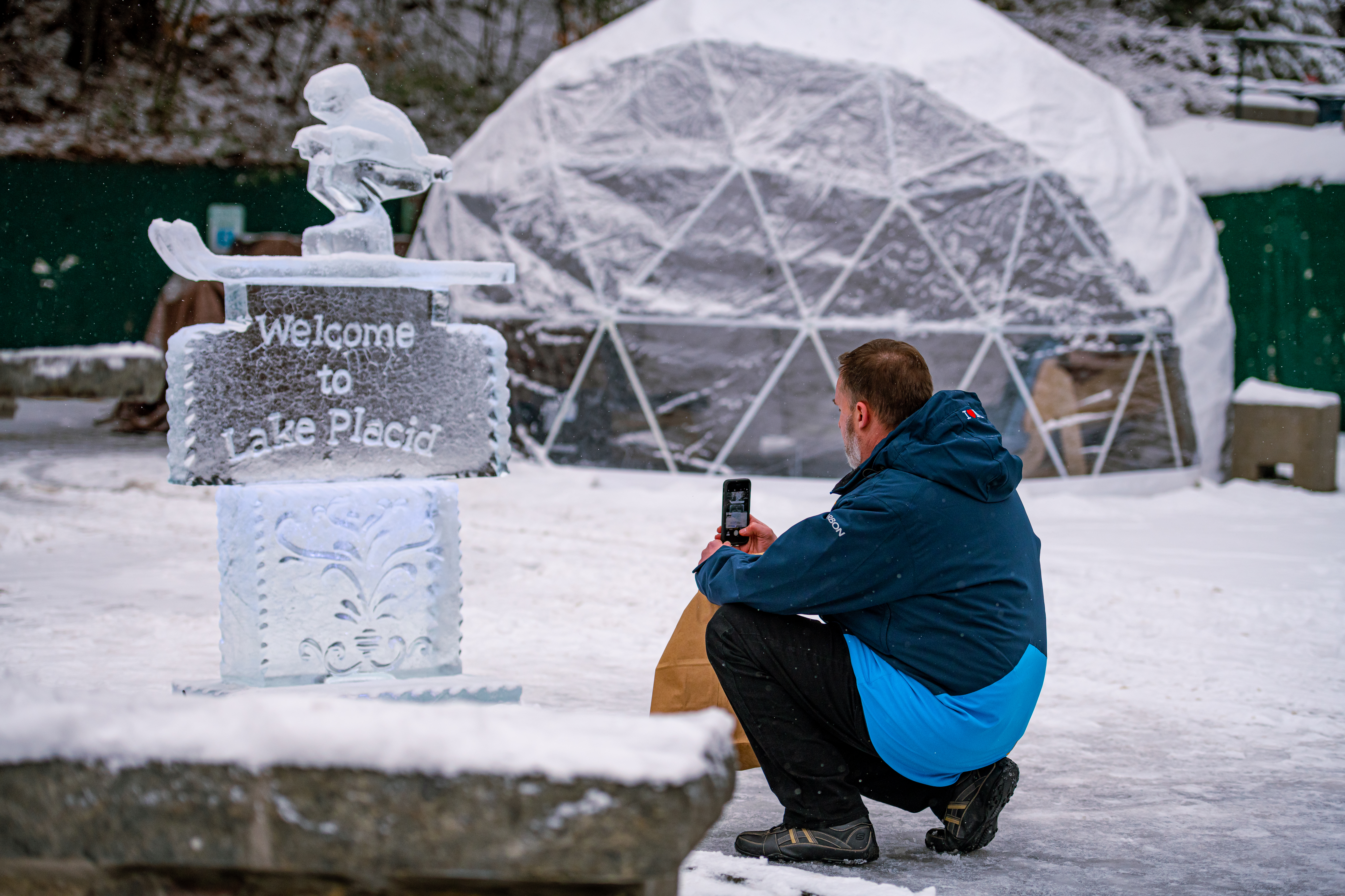 Man takes photo of an ice sculpture with igloo in background