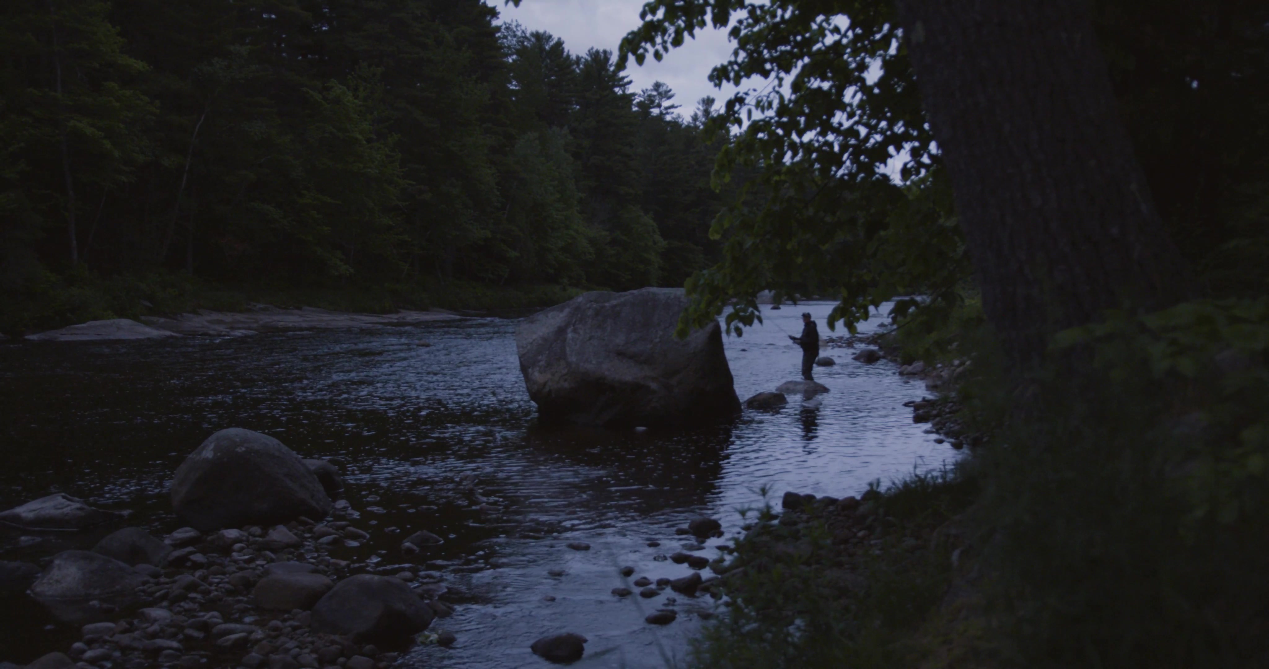 Barely visible in the early morning light, Bottcher stands by a large boulder in the stream.
