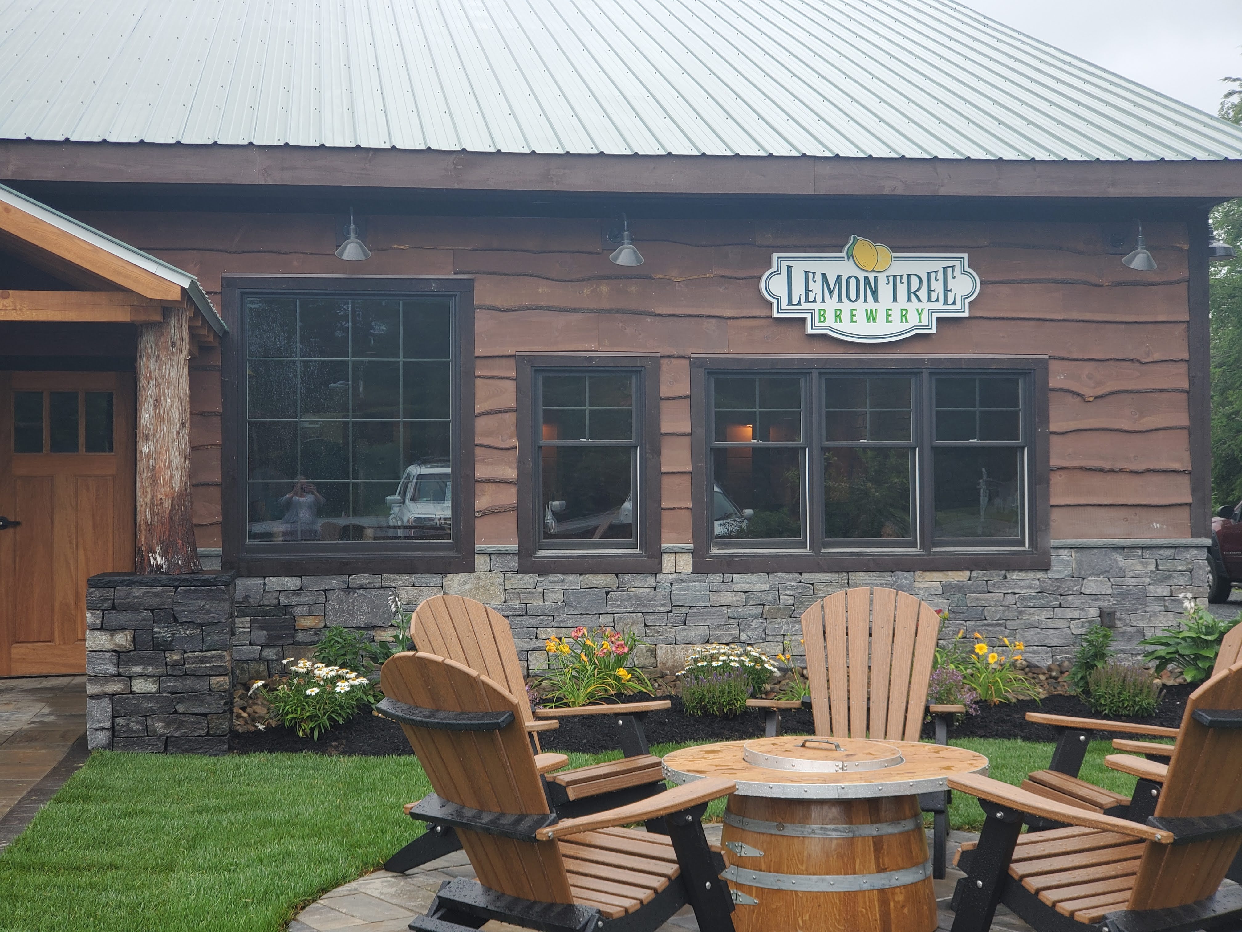 A modern and rustic brown brown building with outdoor seating and Adirondack chairs.