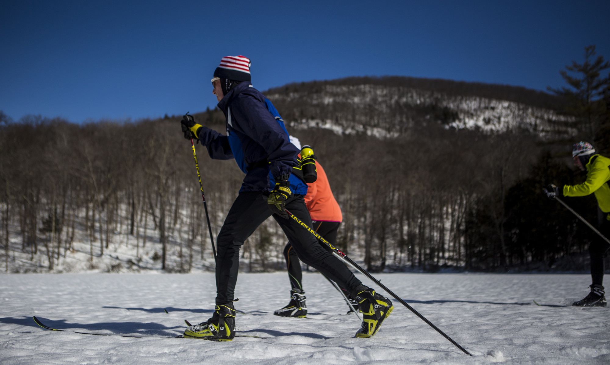 A group of cross-country skiers classic skiing against a blue sky.