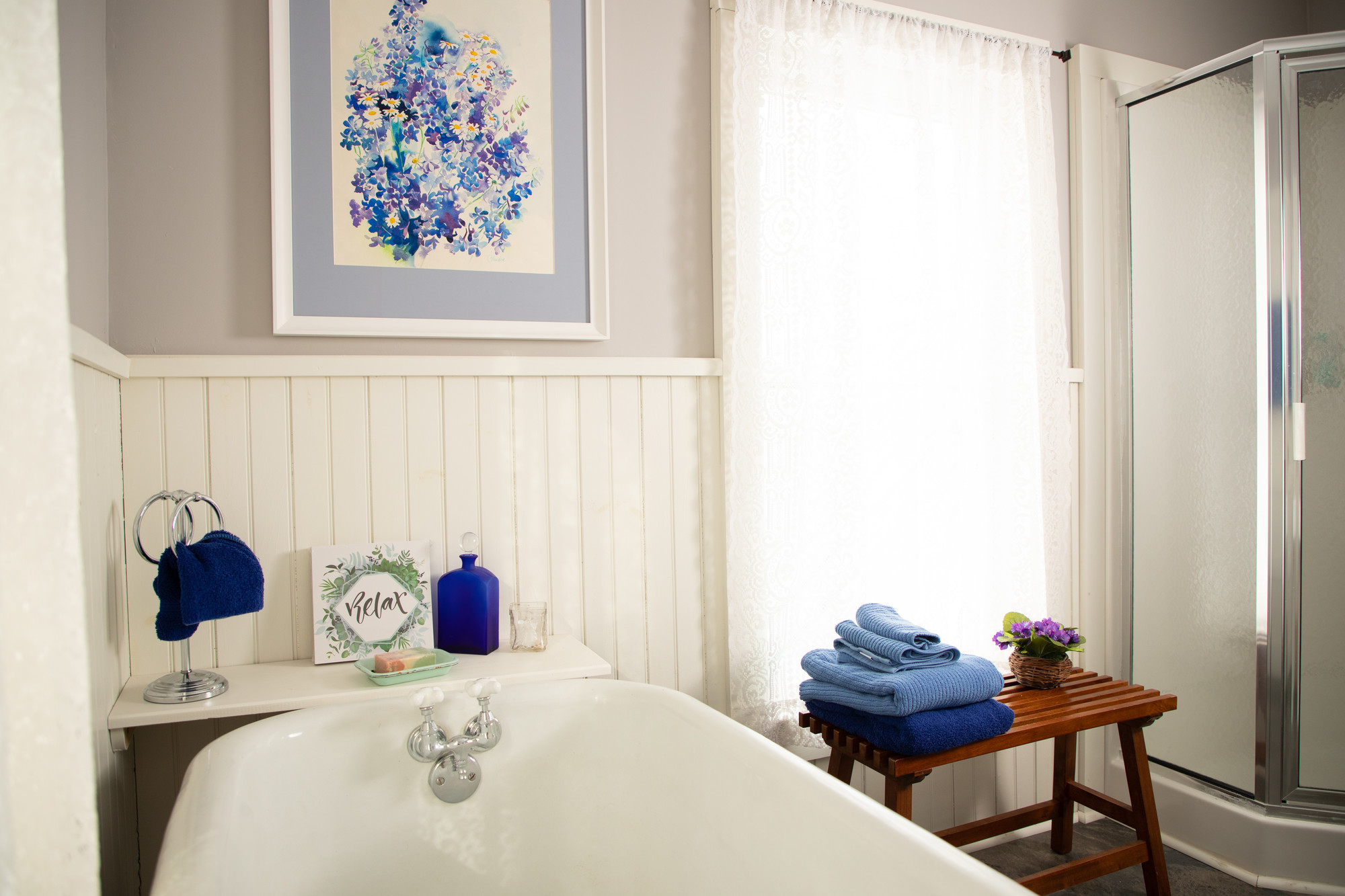 A deep, claw-foot bathtub in a sunlit farmhouse bathroom.