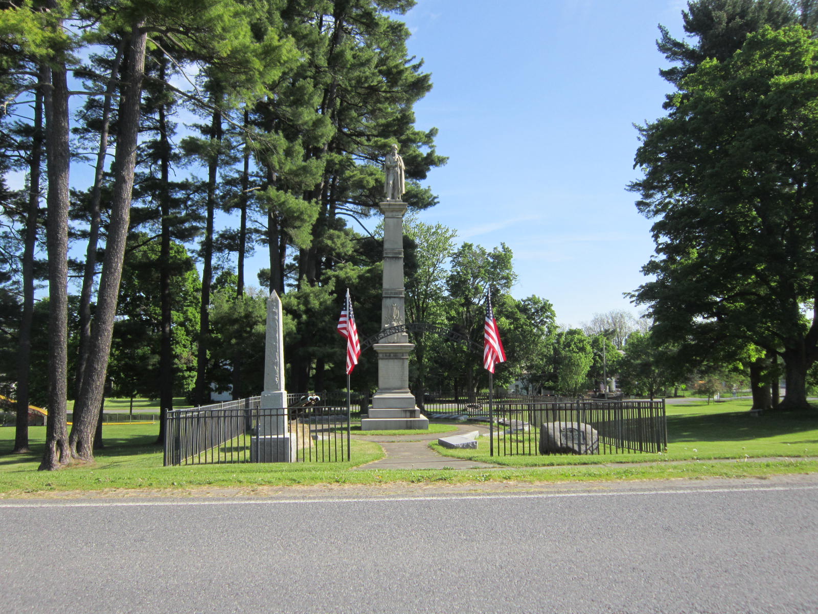 A group of stone obelisks surrounded by an iron fence at a lush green park.