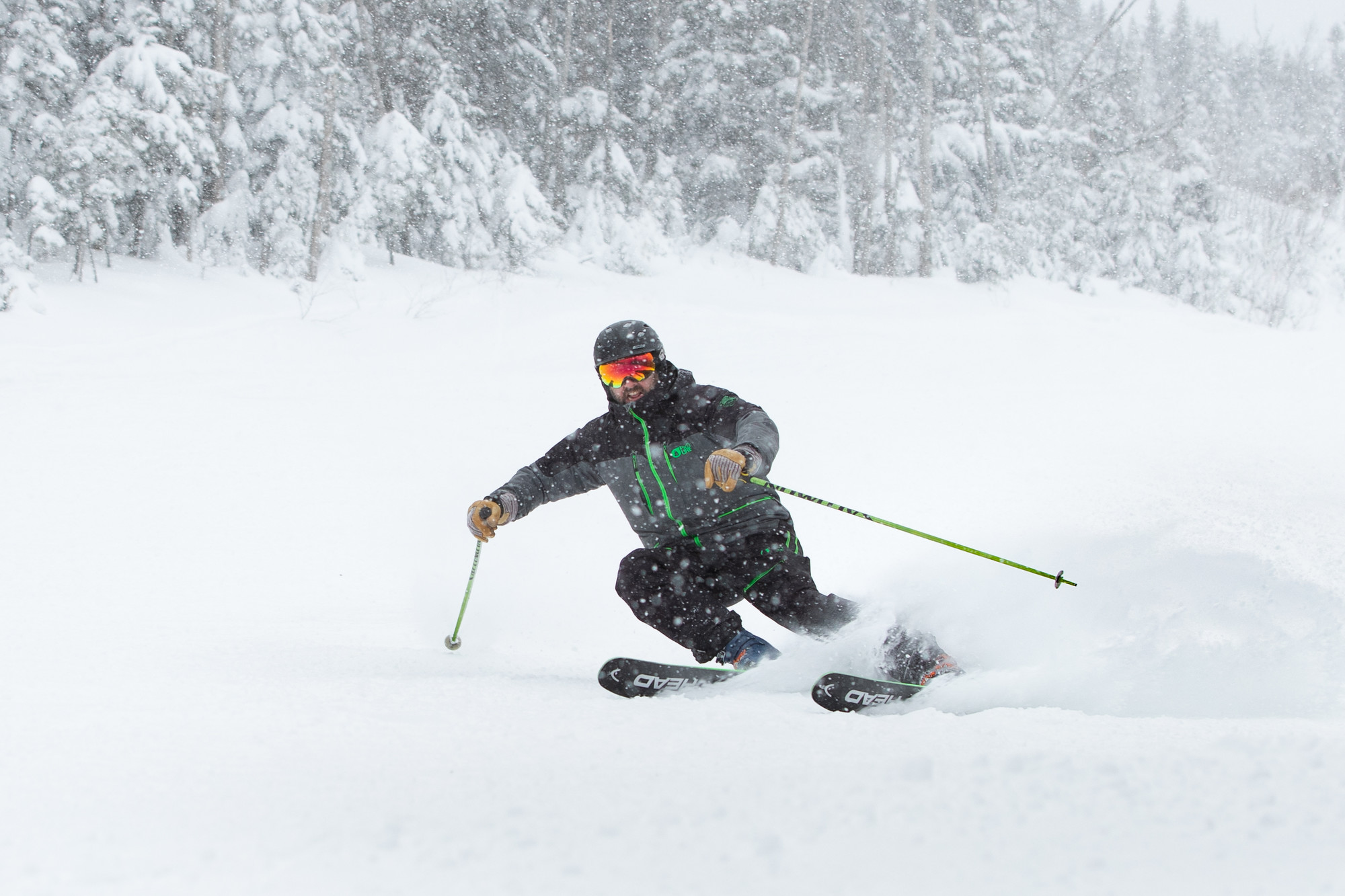 A man in a grey snowsuit skis through the falling snow.