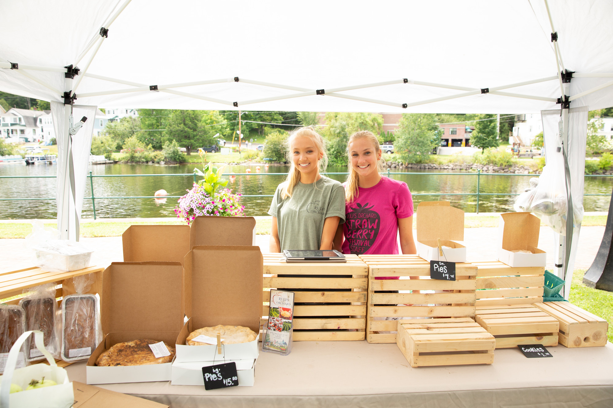 Saranac Lake Farmers Market is a fall experience you can't miss Two girls stand behind their products at the farmers market. Lake Flower and houses serve as the background.