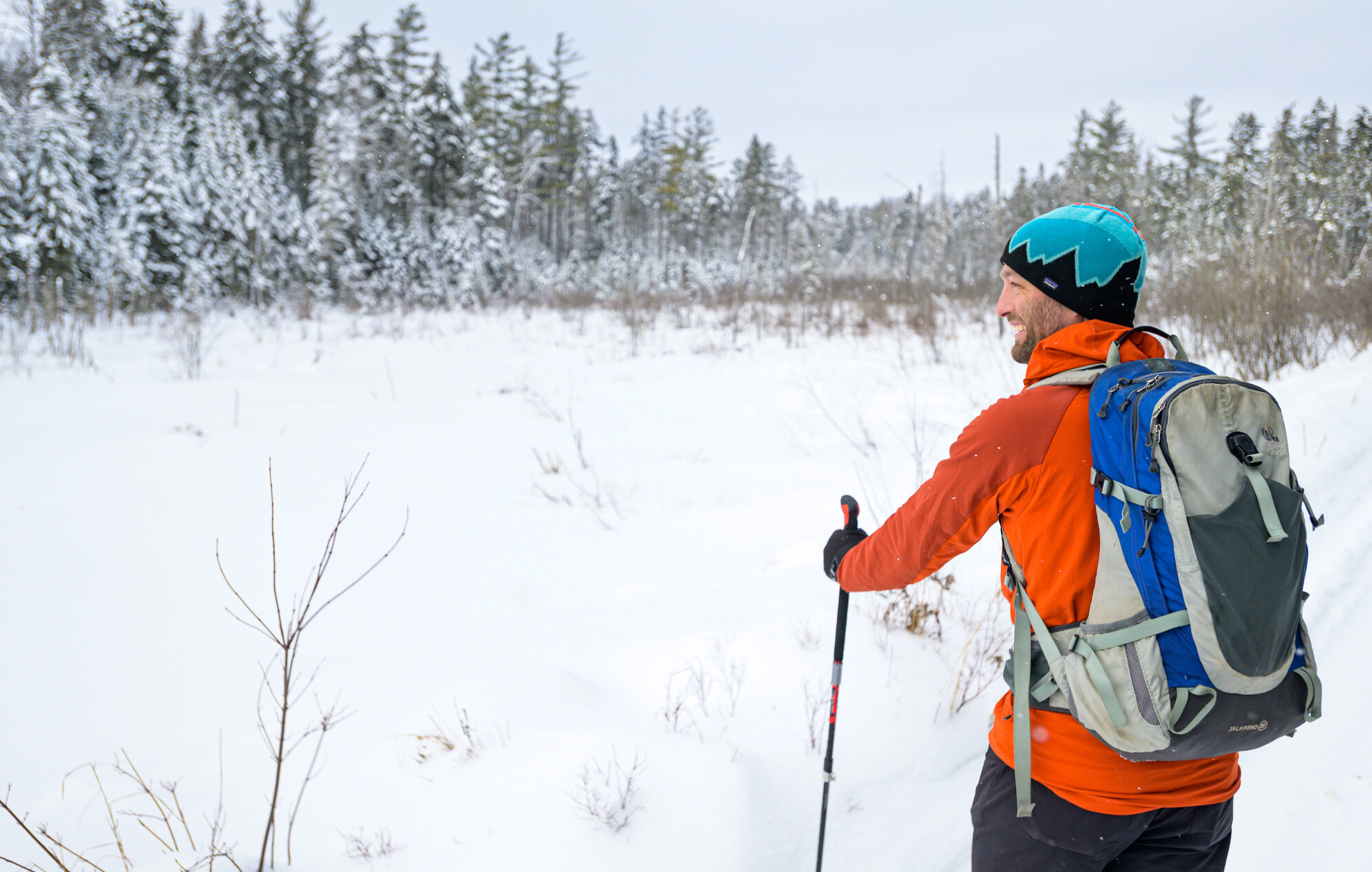 A man in an orange coat smiles on a snow covered trail 