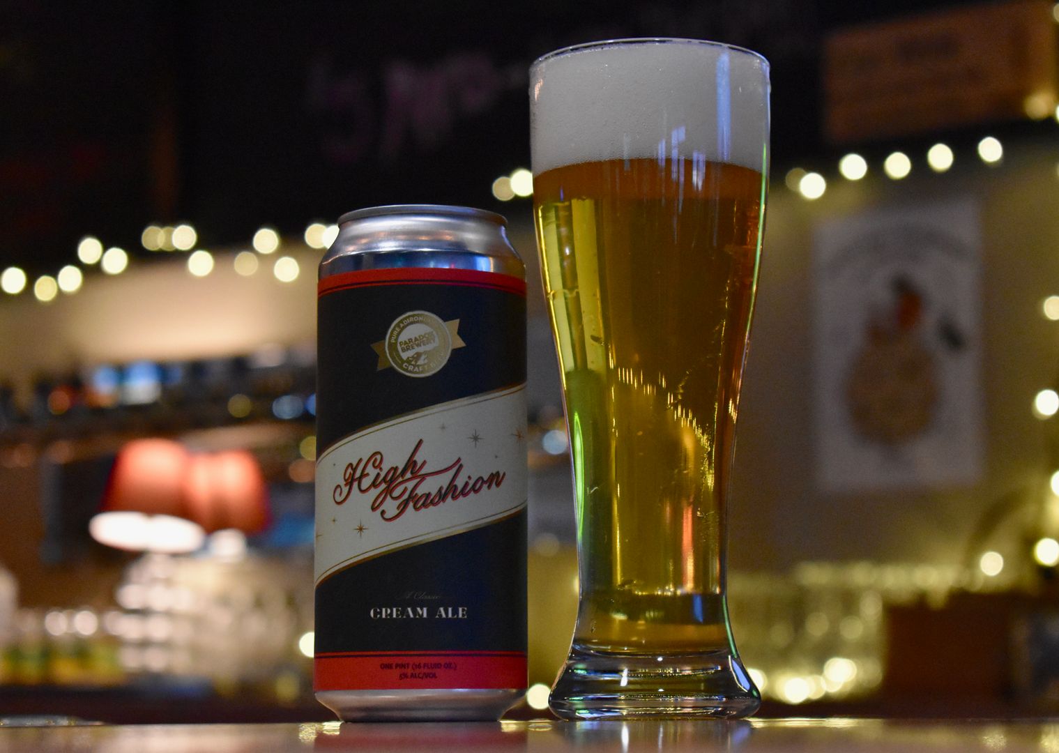 A can of beer sits next to a tall glass full of golden beer on a bar.