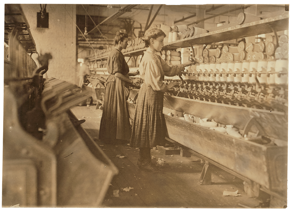 A vintage, sepia-toned photograph of young women at work in a factory in the early 20th century.