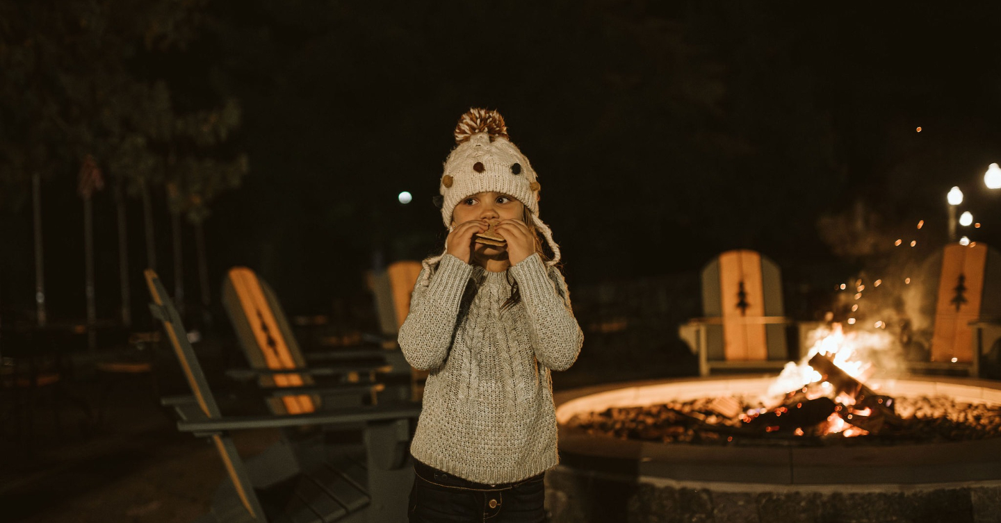A child stands near a fire at The Lodge at Schroon Lake and eats a s'more 