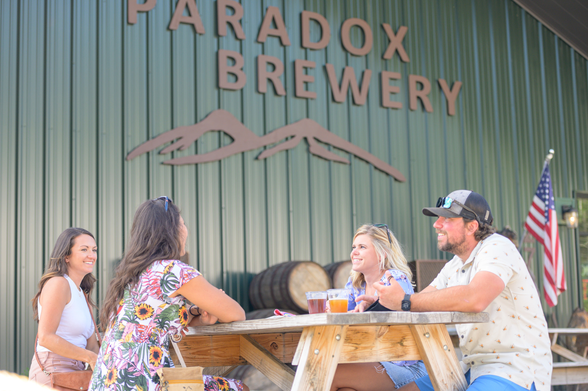 A group of friends sit at a picnic table at a brewery. 