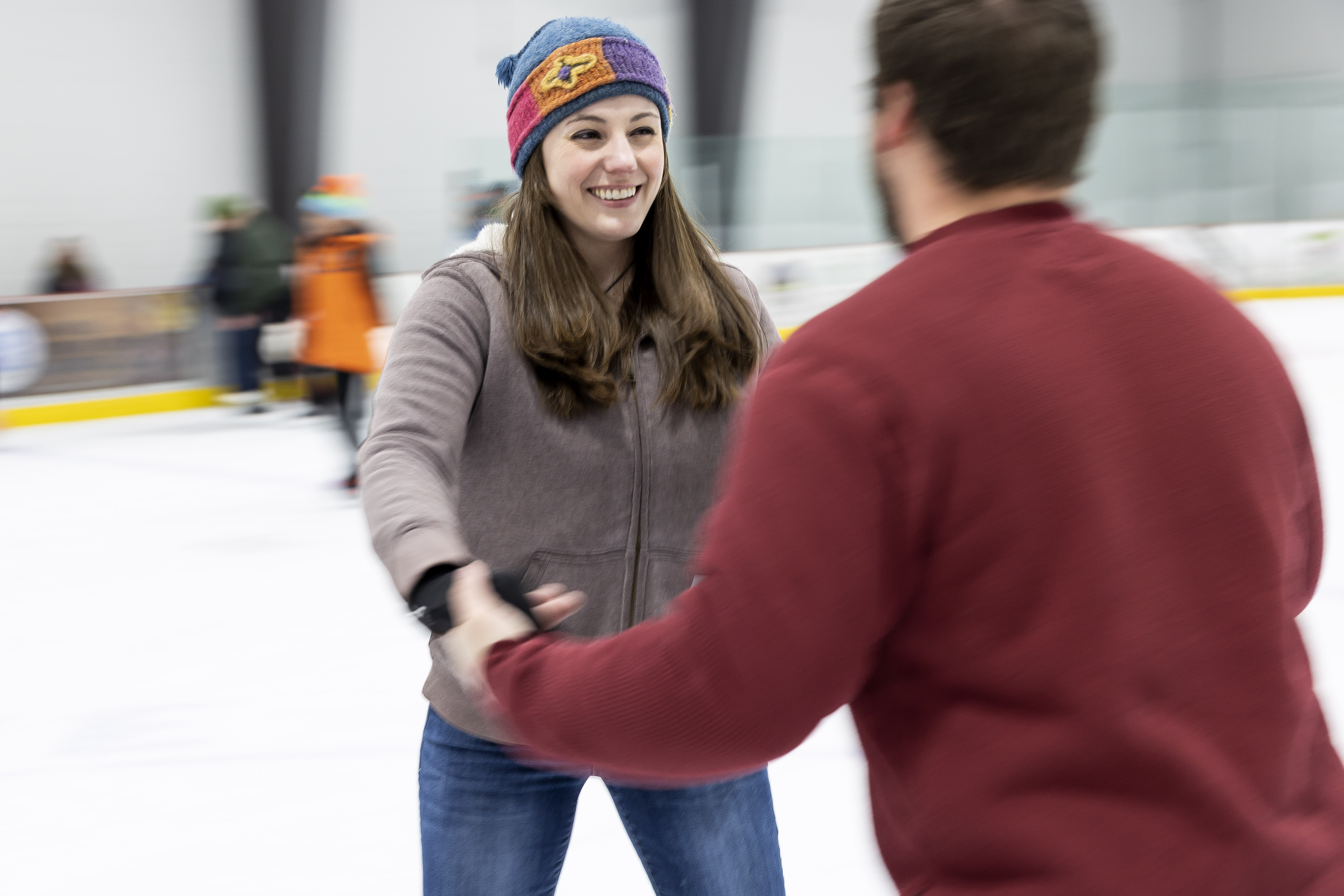 A man and woman laugh as they skate holding hands.