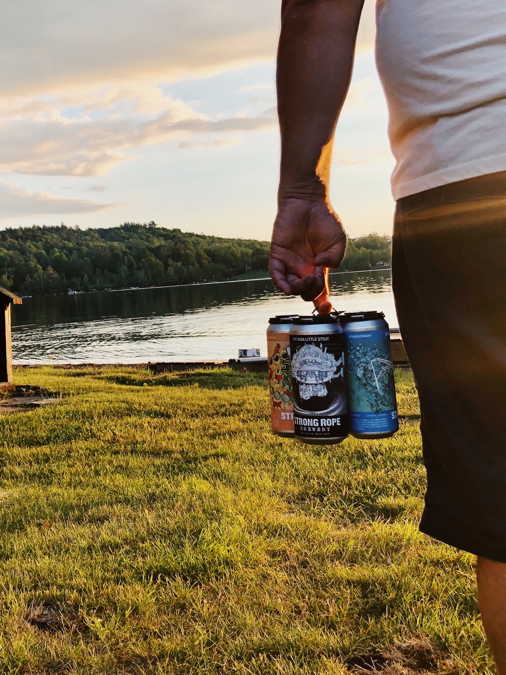 Close up of a man holding a Strong Rope four-pack by the shore of a lake.