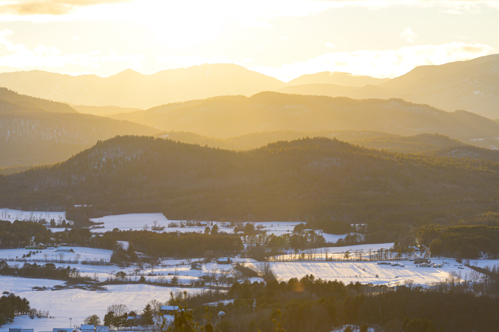 The sun sets over the mountains, surrounded by snow covered fields