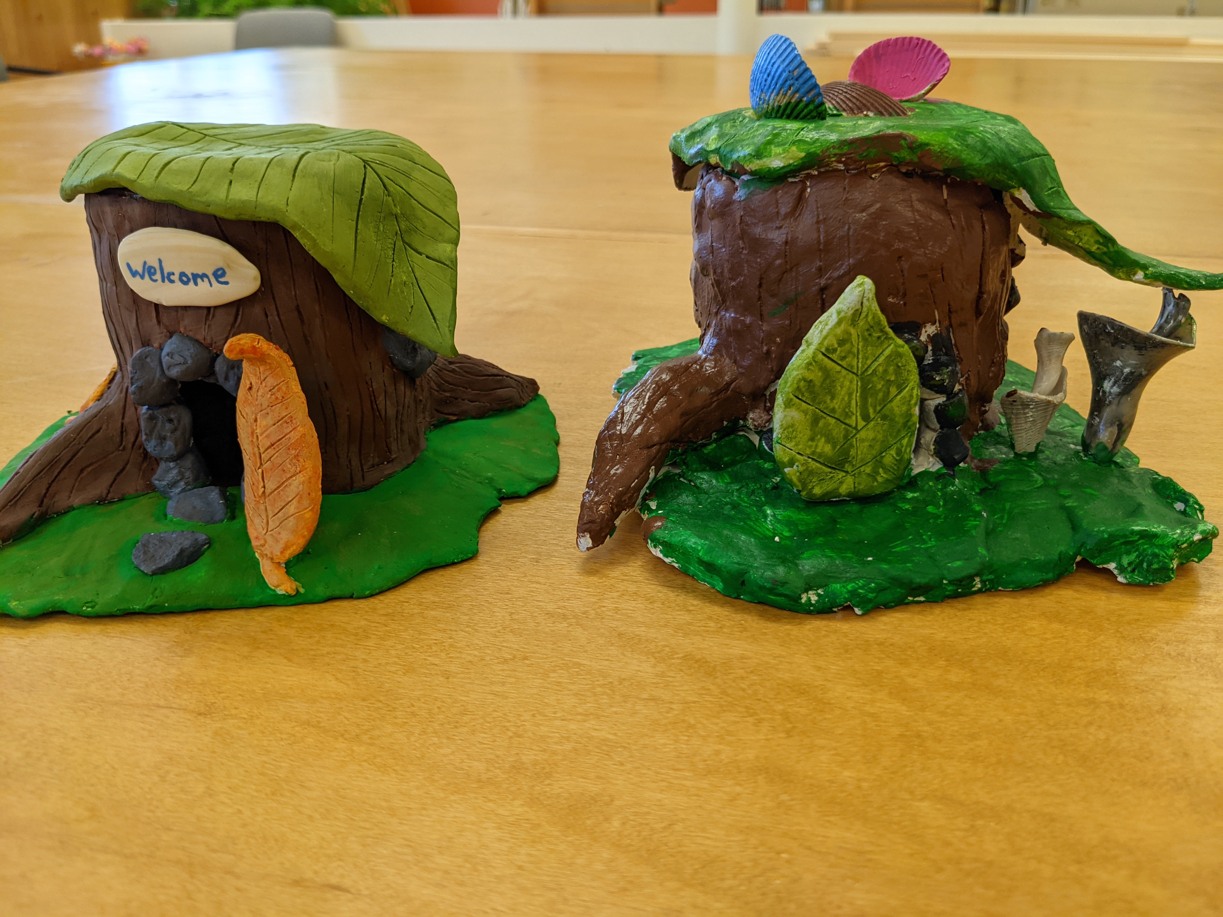 A clay hut created by a child is placed next to the teacher's clay hut