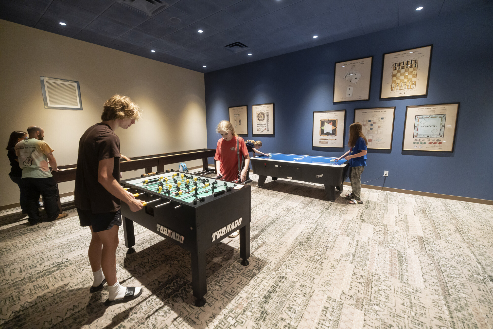 People play air hockey and foosball games in a hotel game room.