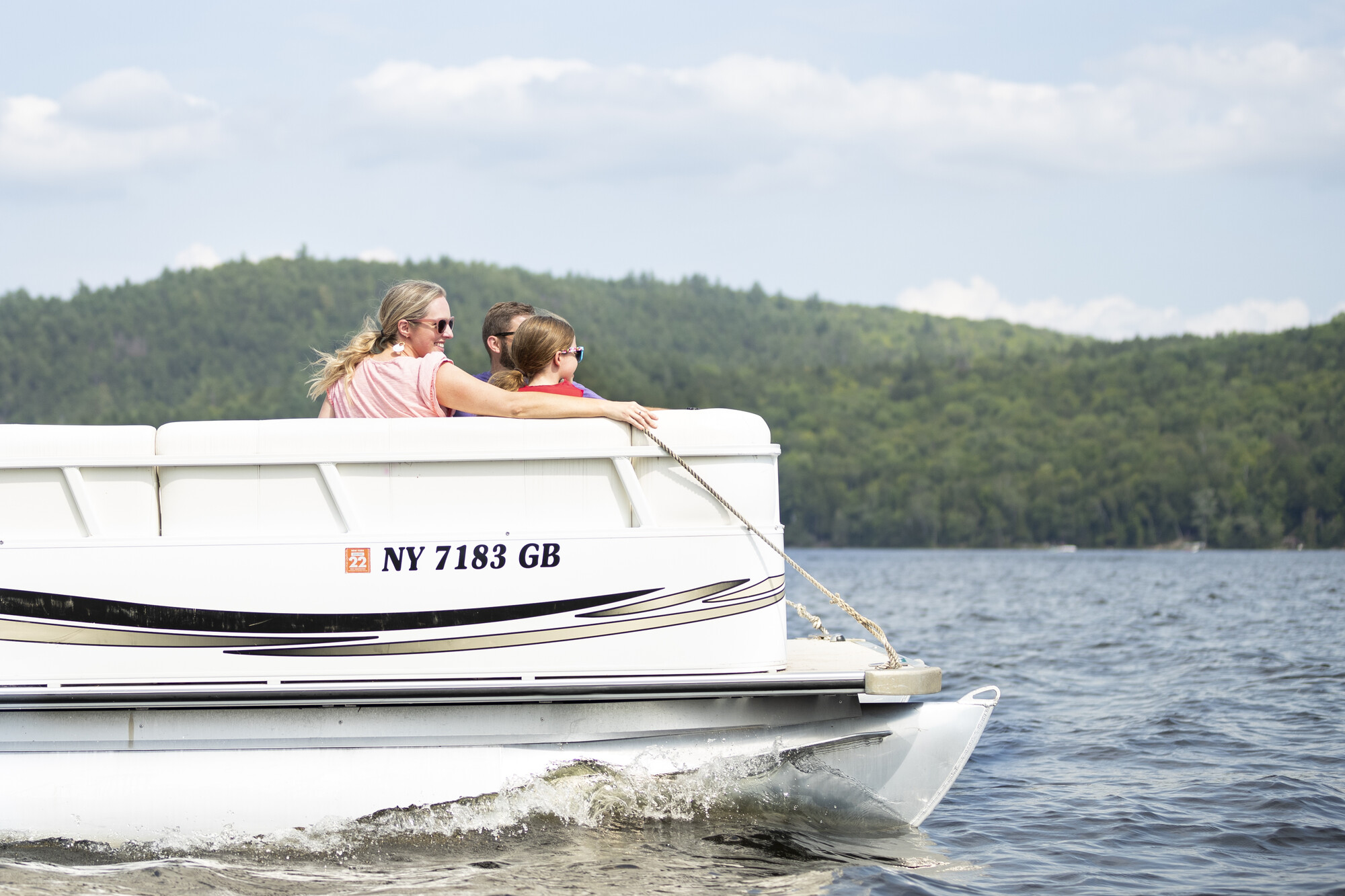 A woman and two children sit on a moving pontoon boat.