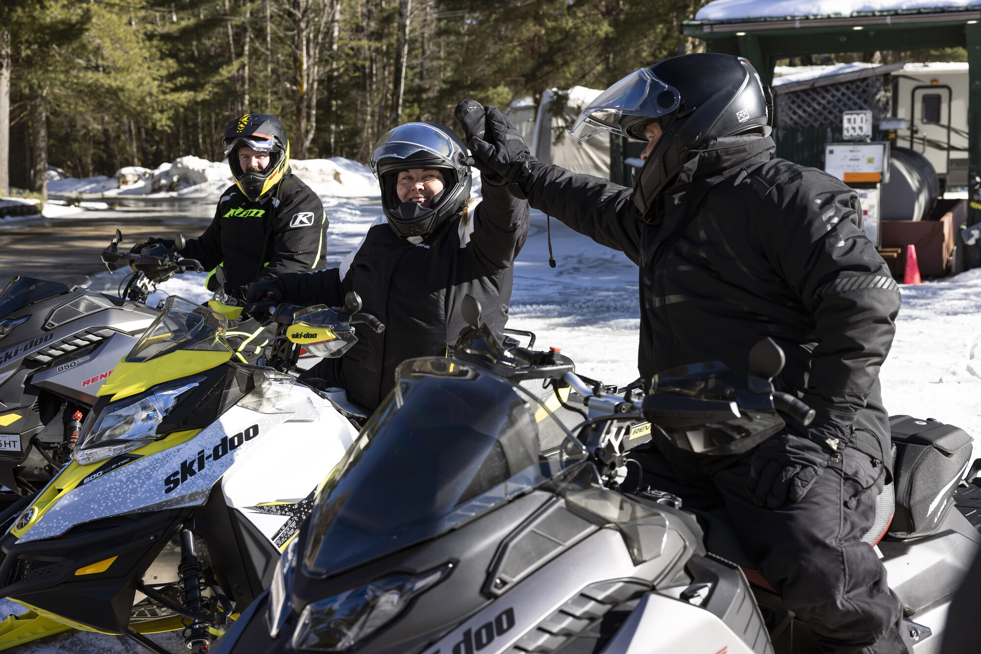 A man and woman high five on their snowmobiles. 