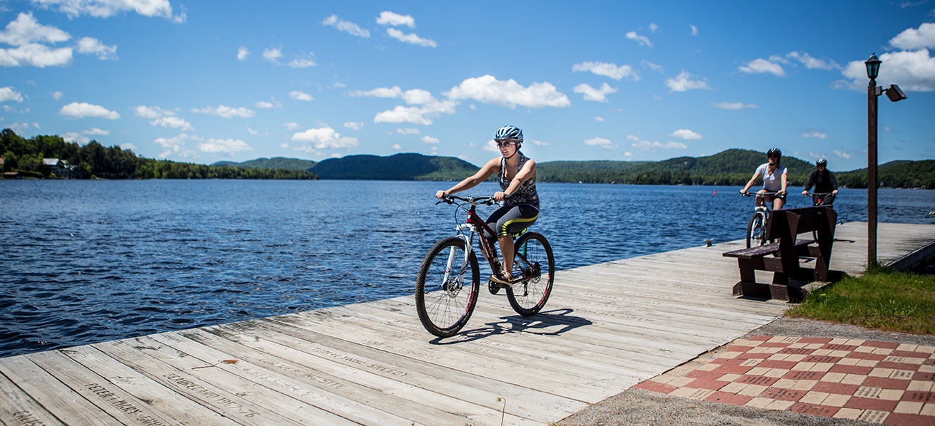 Three adults bicycle on a wooden pier next to a lake.