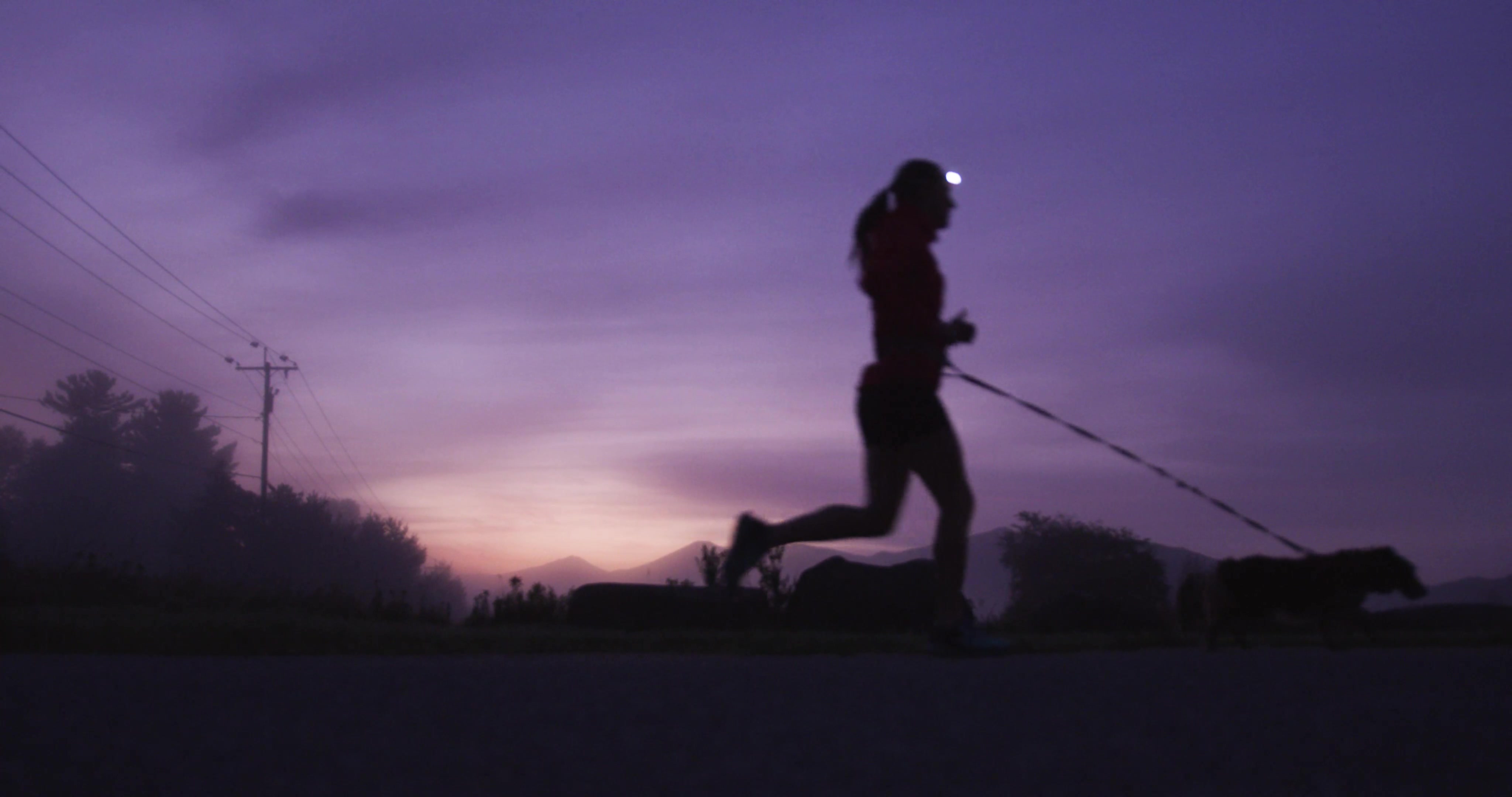 The silhouette of a woman running in front of the mountains at dawn