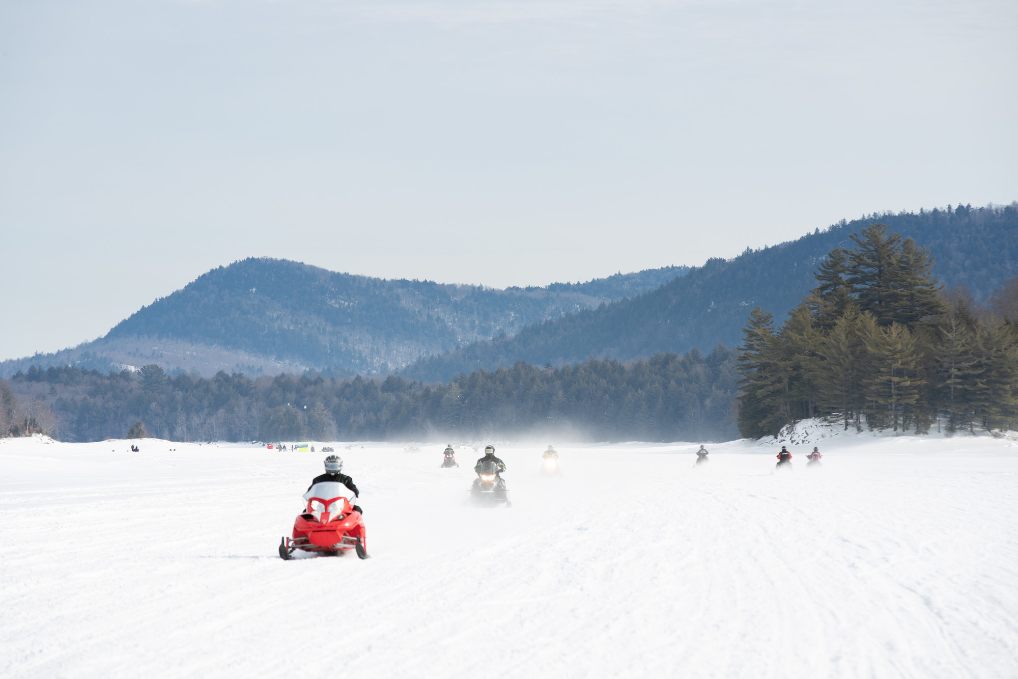 A group of people snowmobile across a frozen lake. 