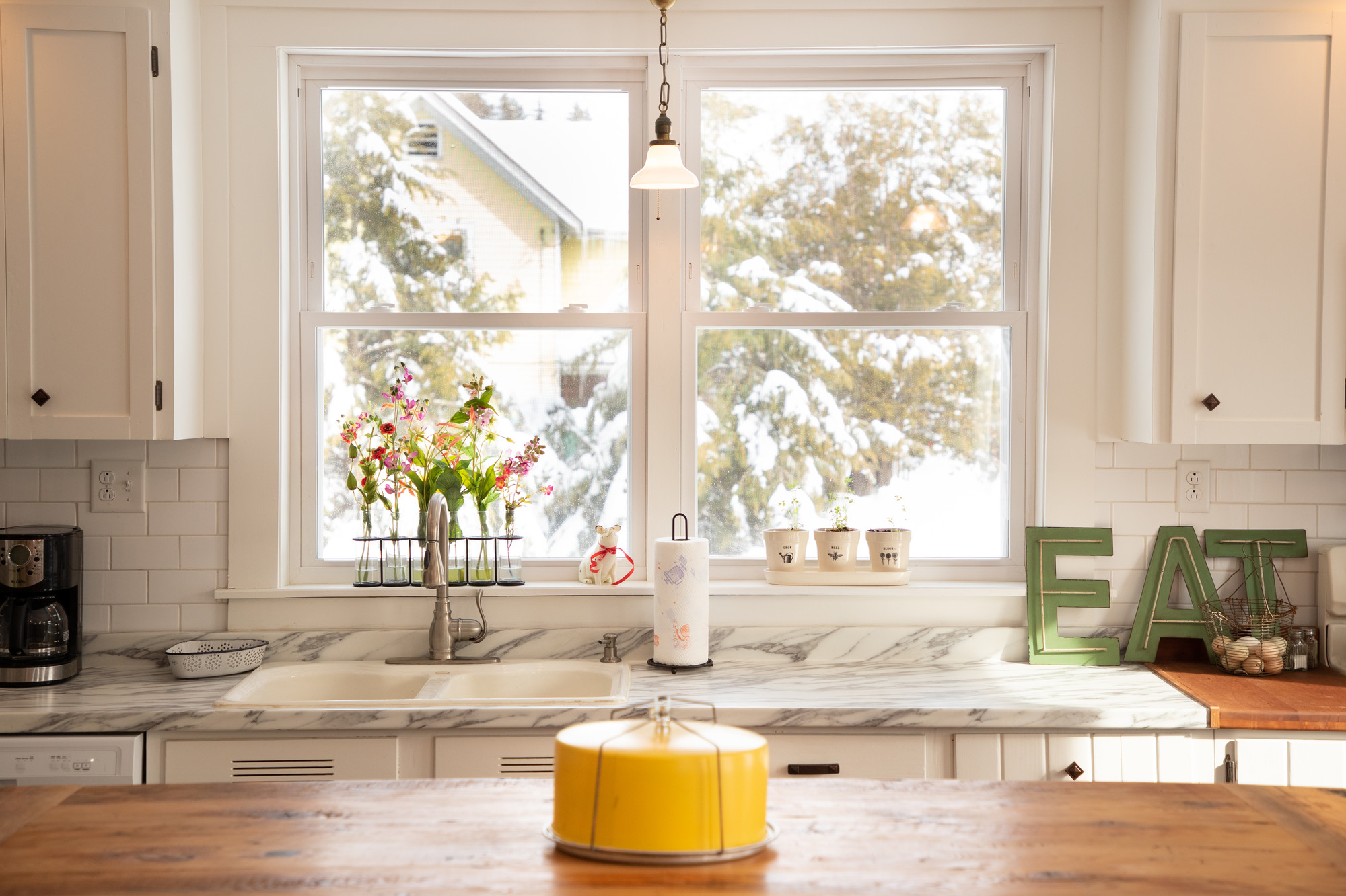 a sink and white granite counter in front of a large window looking out at snow.
